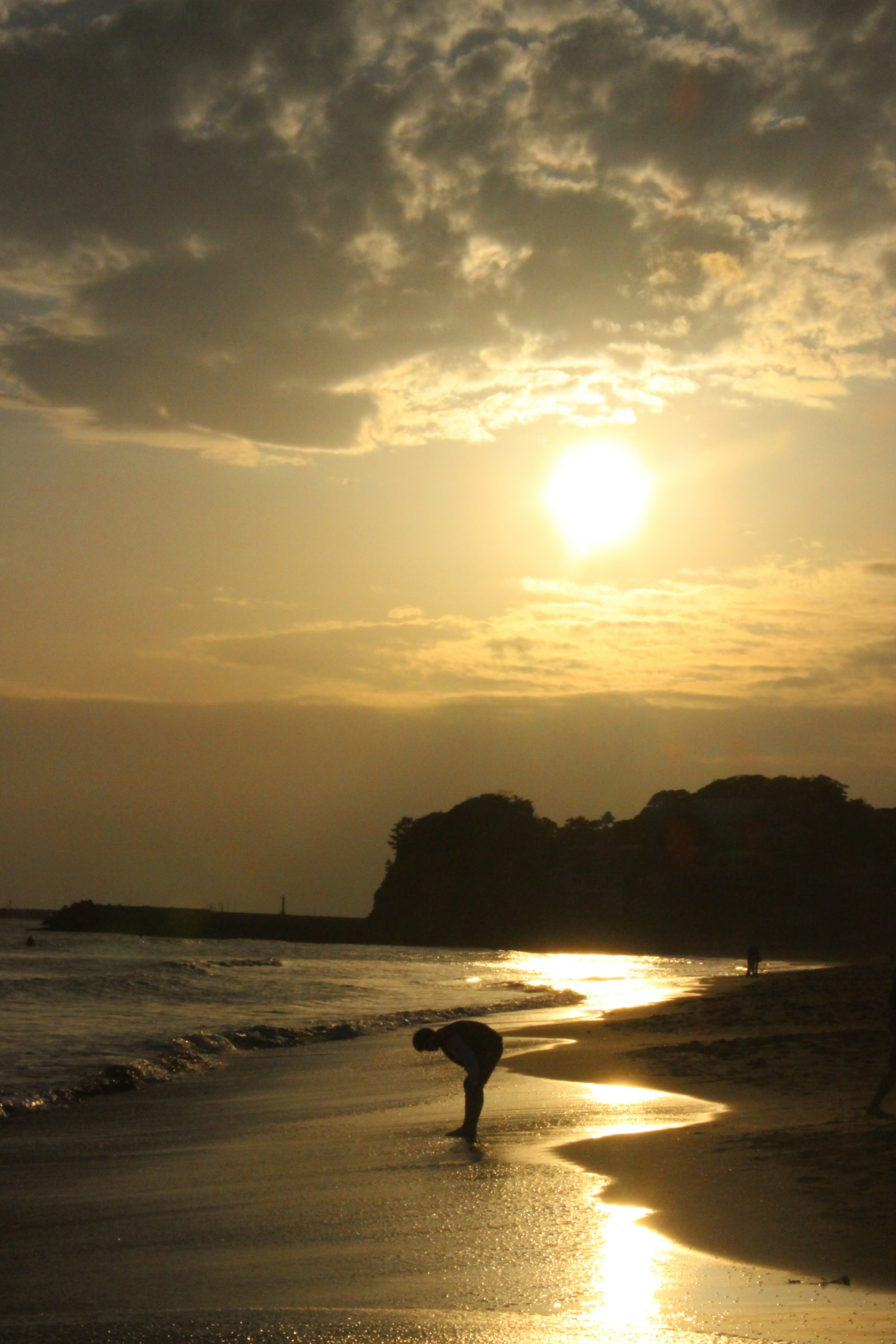 夕日を背に砂浜で曲がっている人物のシルエット