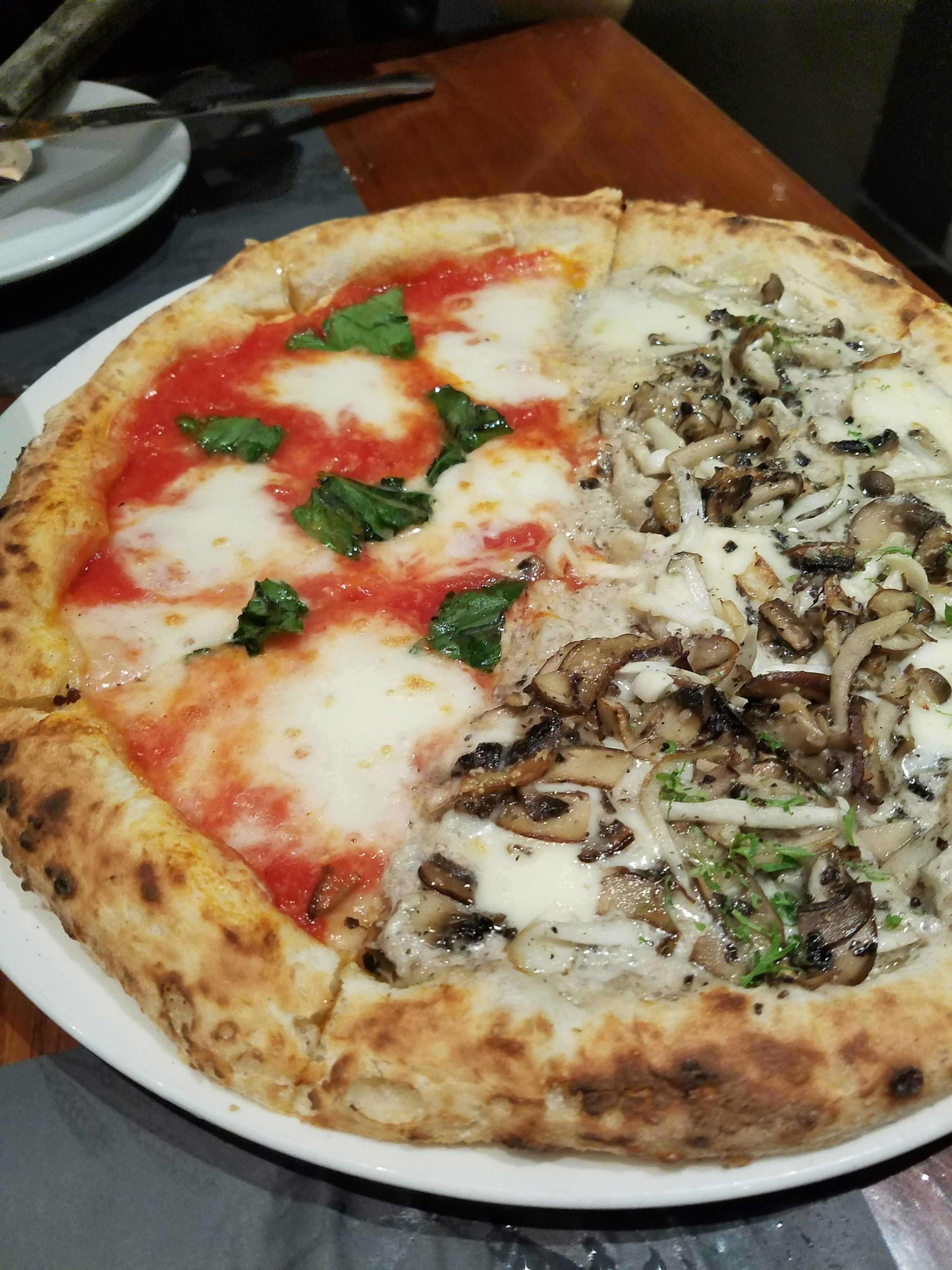 Pizza metà Margherita con mozzarella e basilico metà funghi con salsa bianca