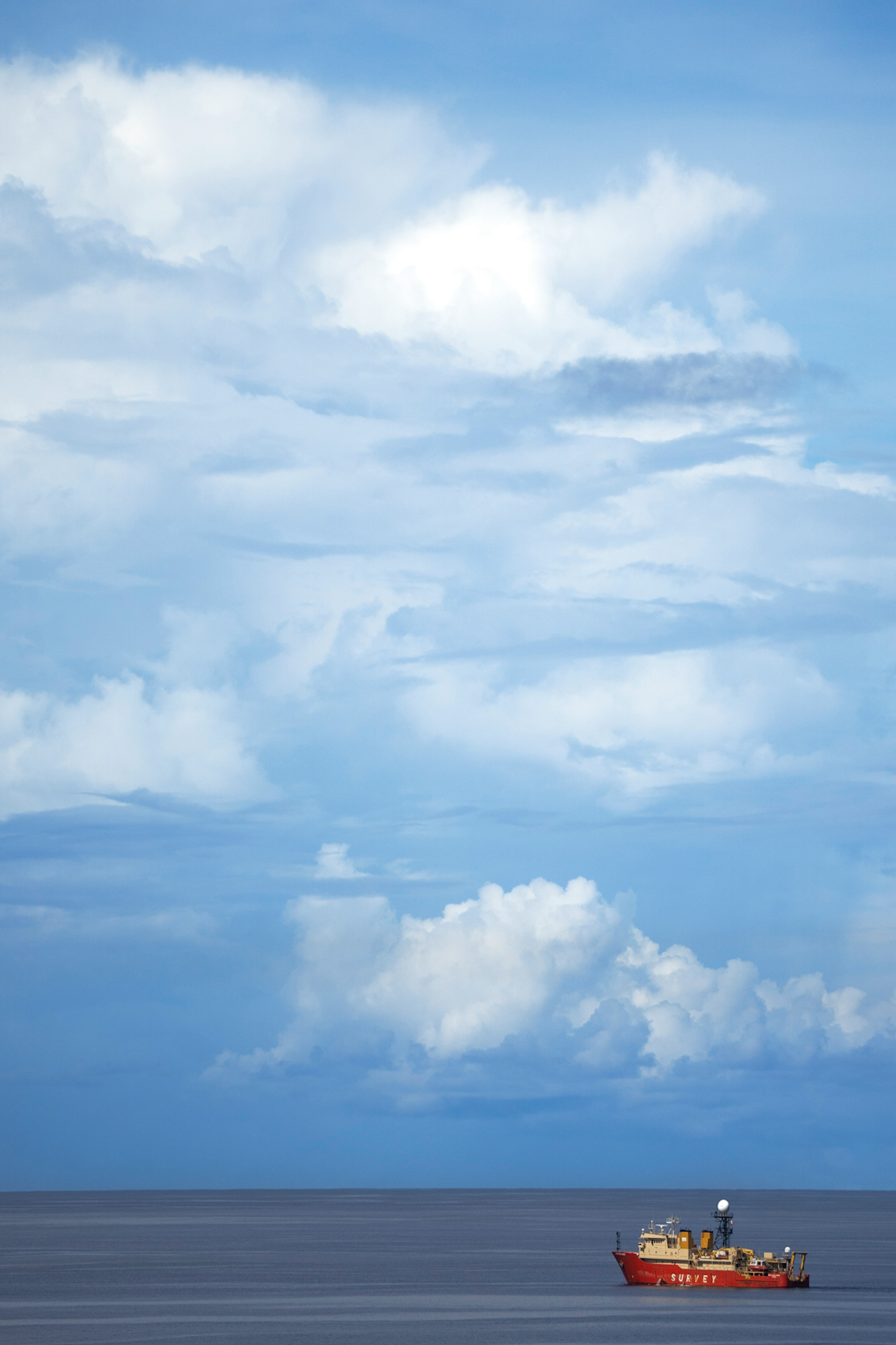 青い空と白い雲の下に浮かぶ赤い船