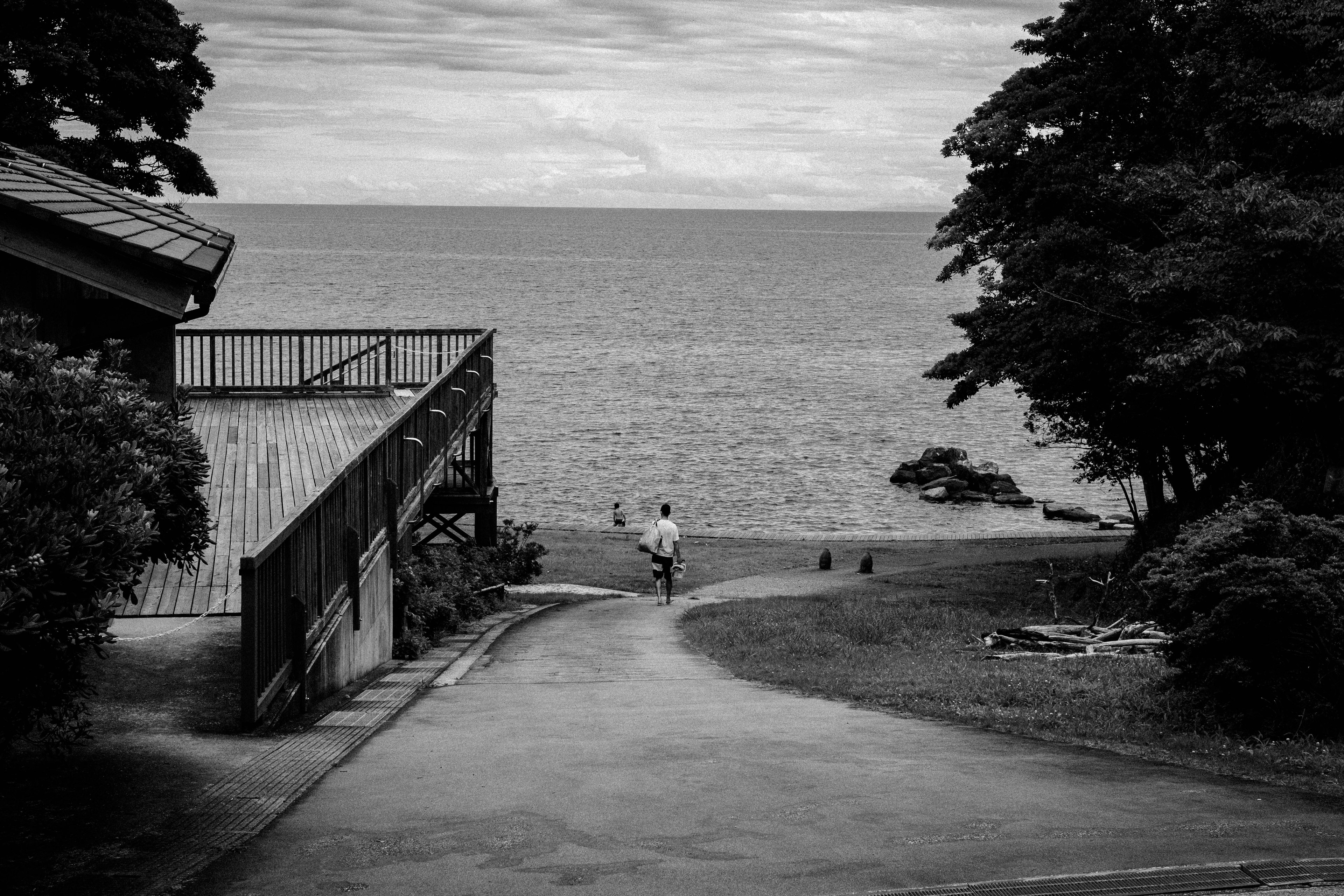 A person walking towards the sea with a wooden structure nearby