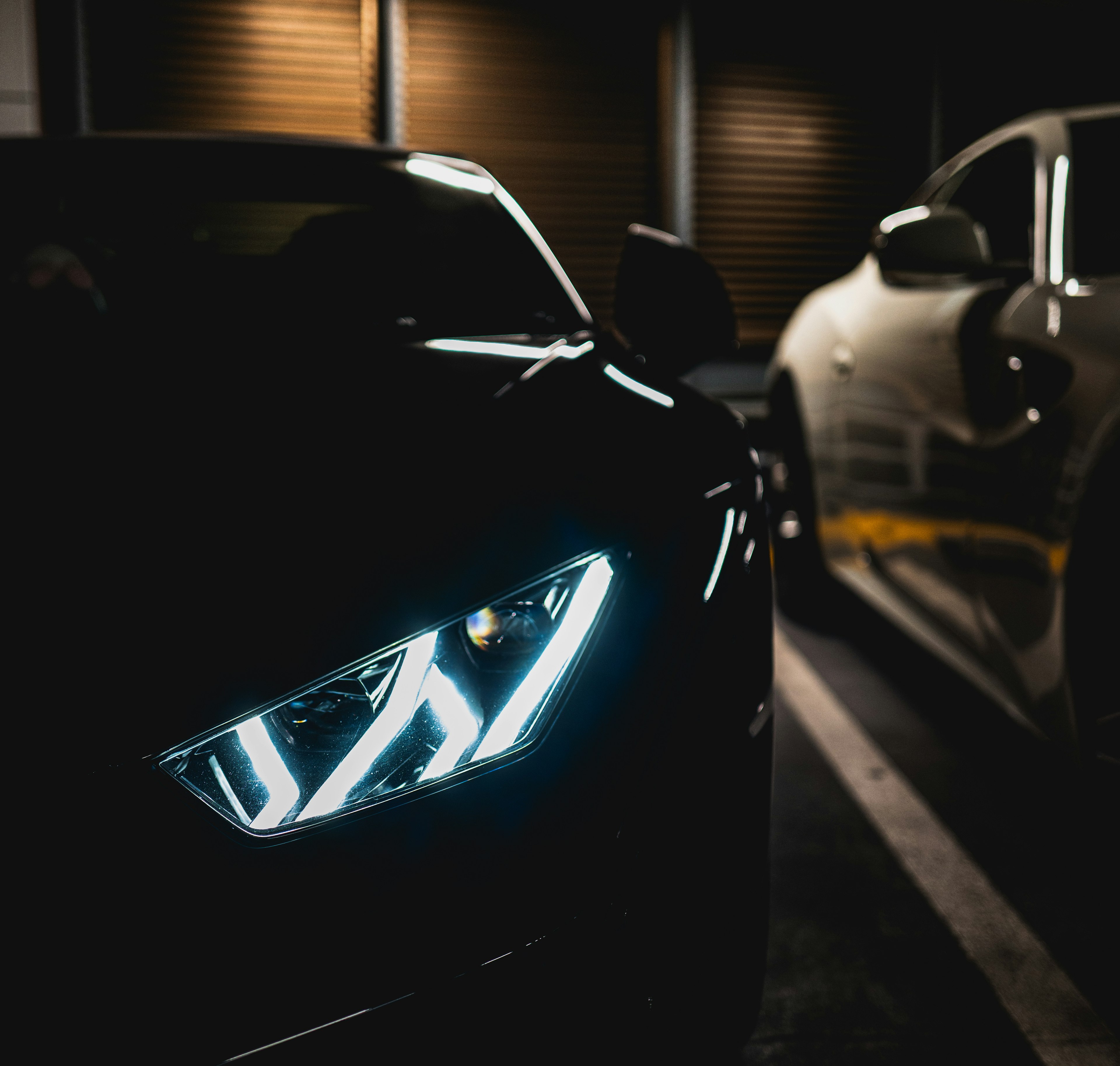 Close-up of a black car's headlight in a dark parking lot