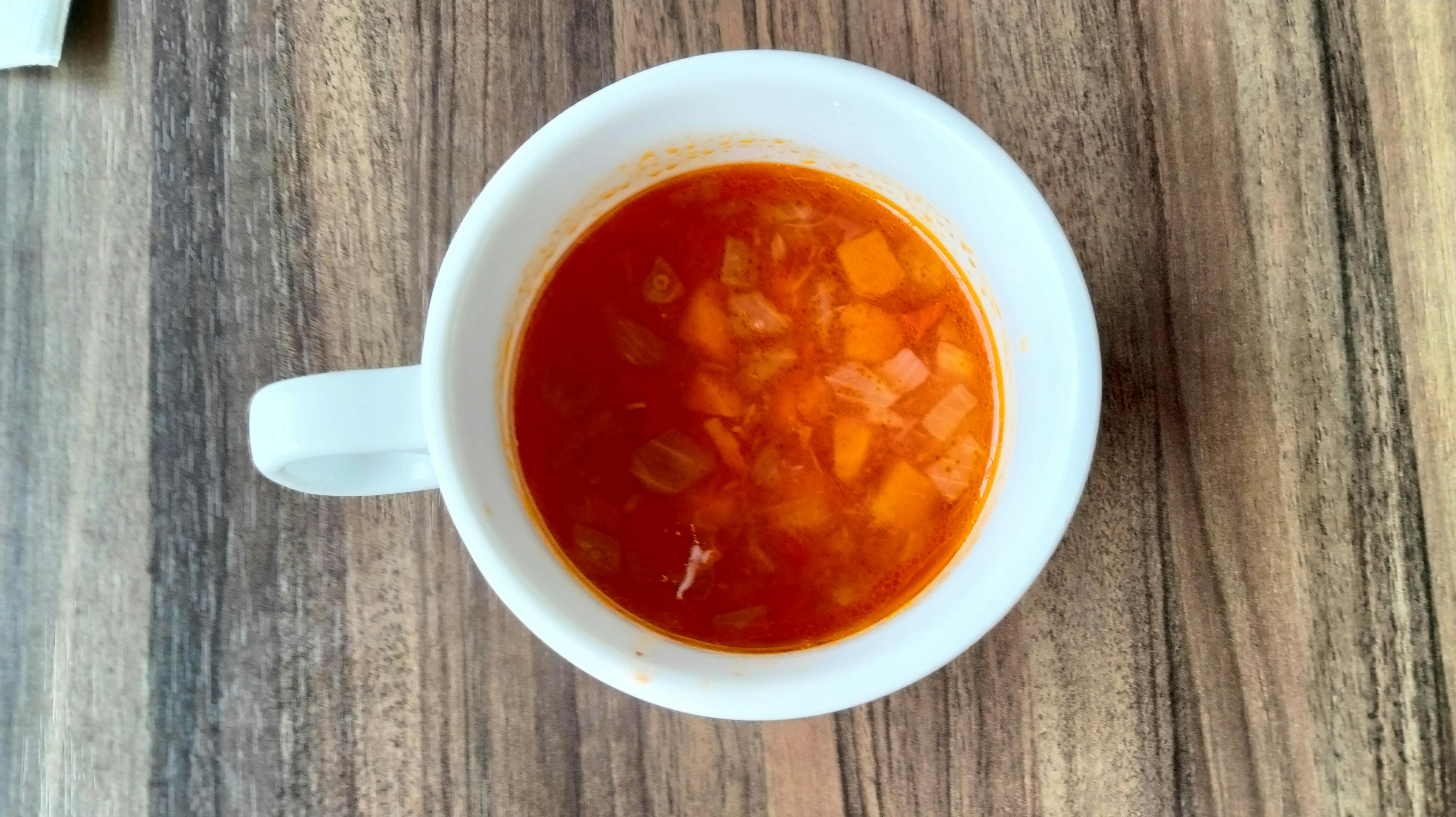 Orange Suppe mit gewürfeltem Gemüse in einer weißen Tasse