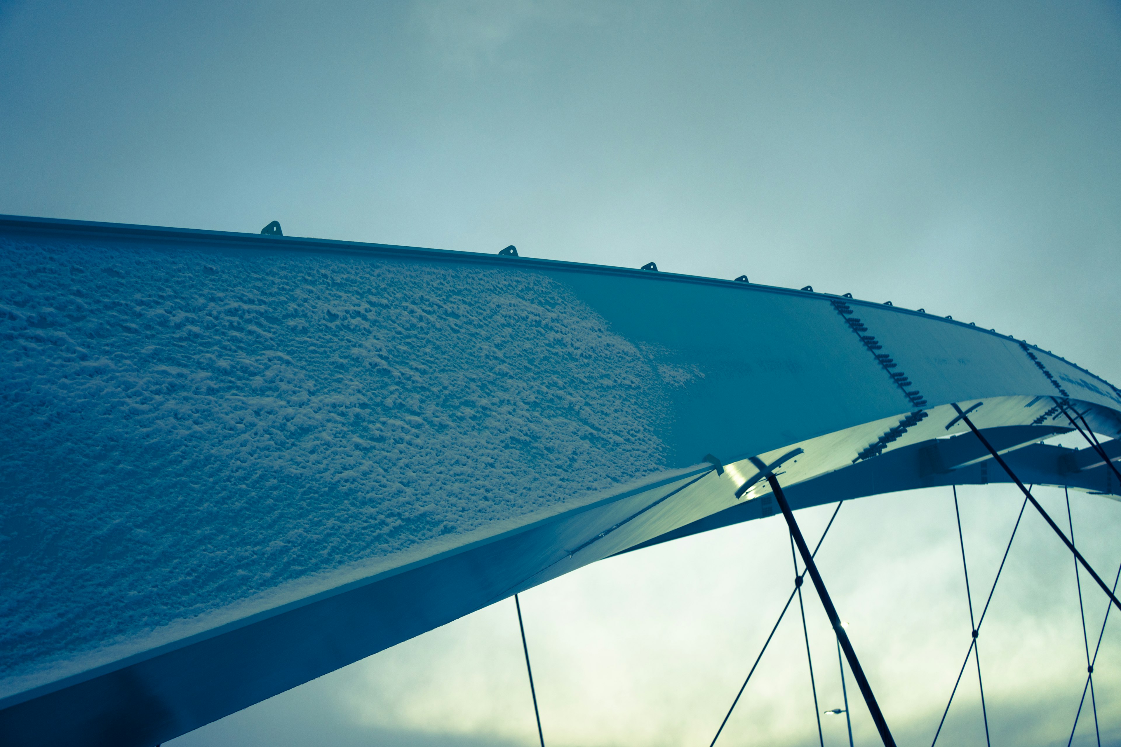 Primer plano de un arco de puente azul reflejando el cielo y la textura metálica