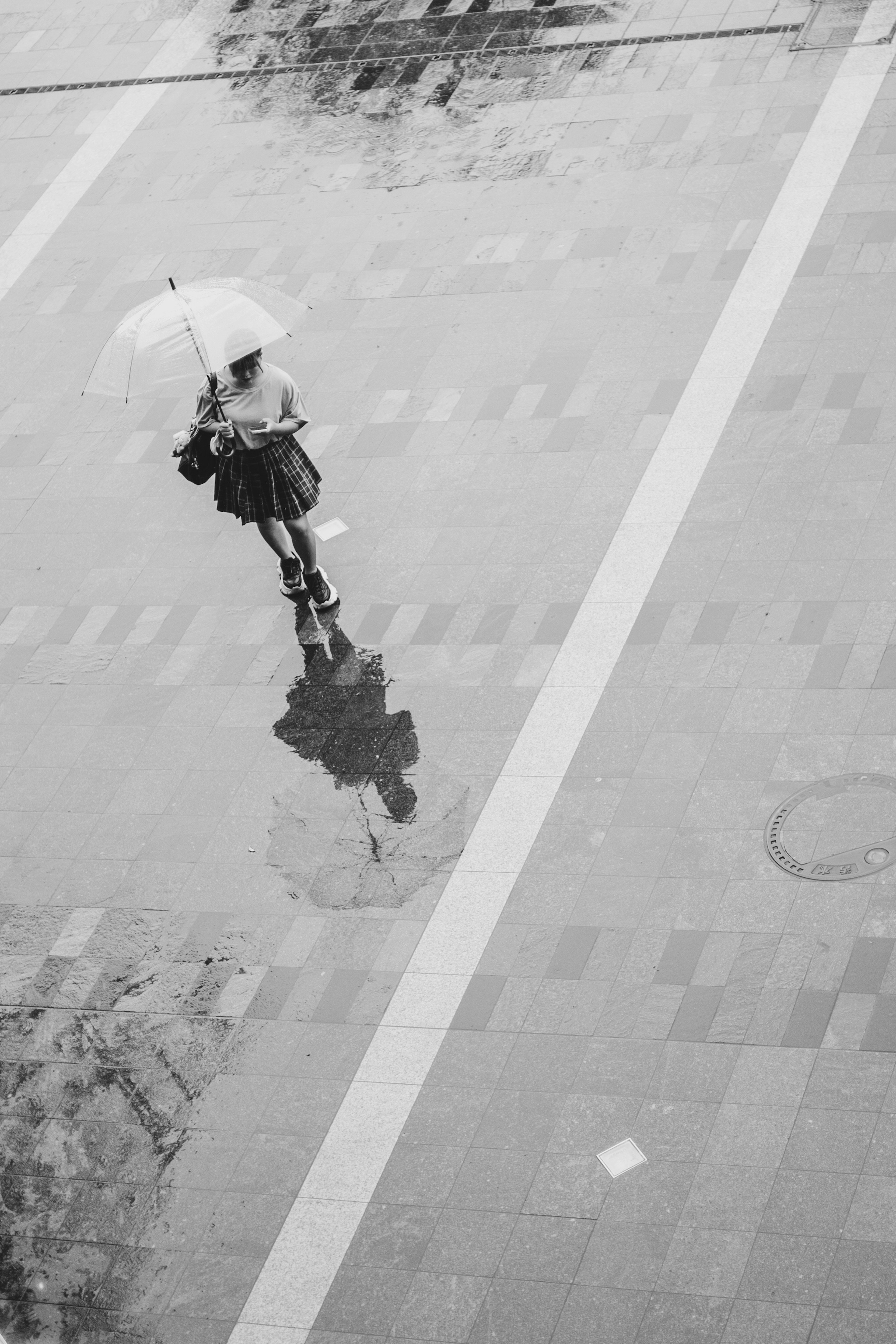 Black and white image of a woman walking with an umbrella in the rain