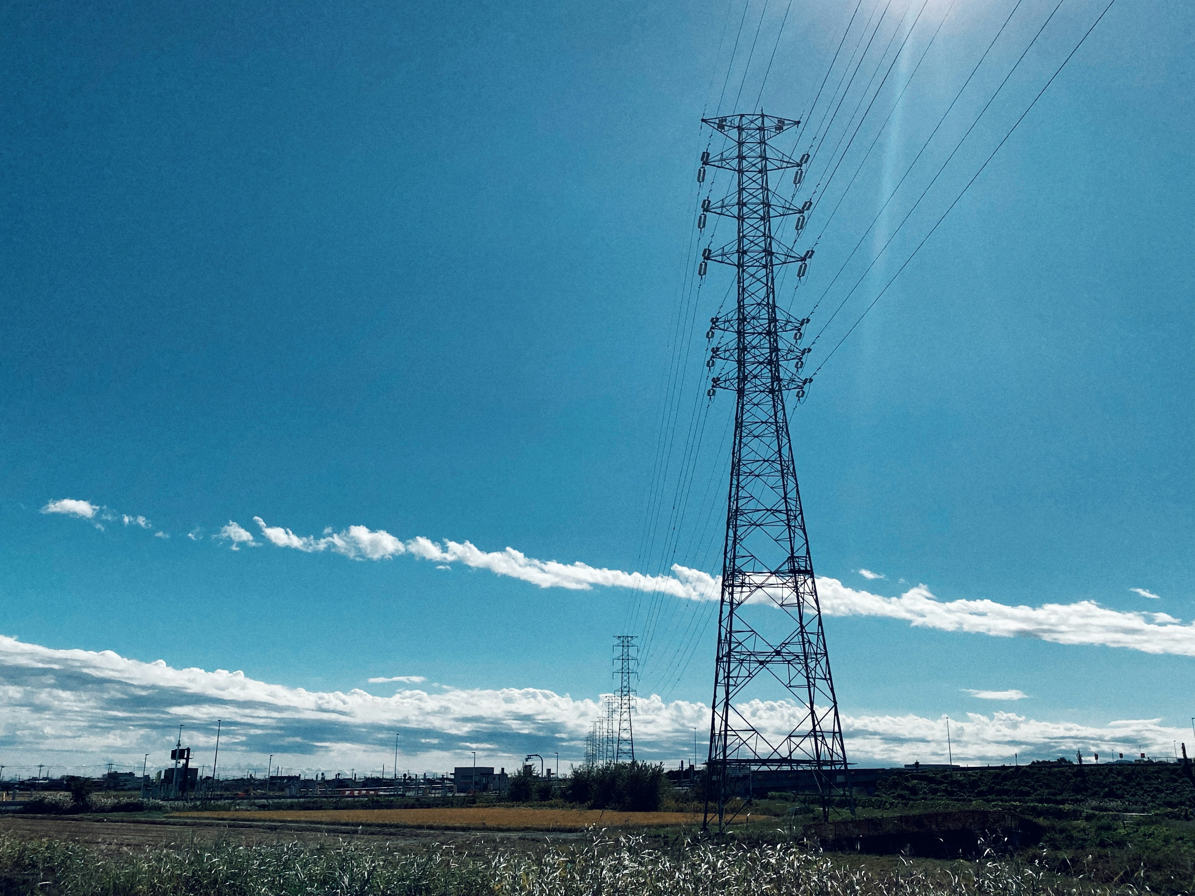 Torre elettrica ad alta tensione sotto un cielo blu con nuvole bianche