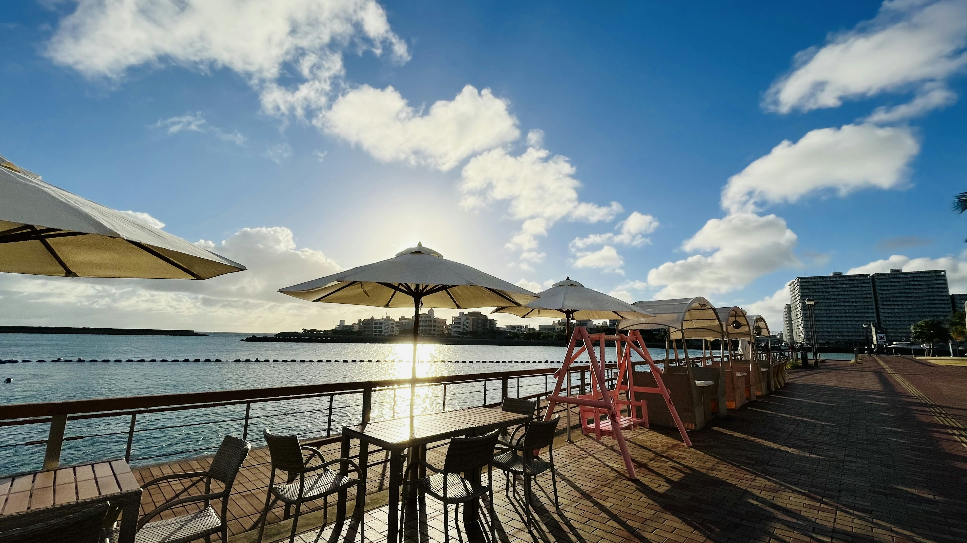 Seaside café terrace with umbrellas overlooking a sparkling blue sky and sun