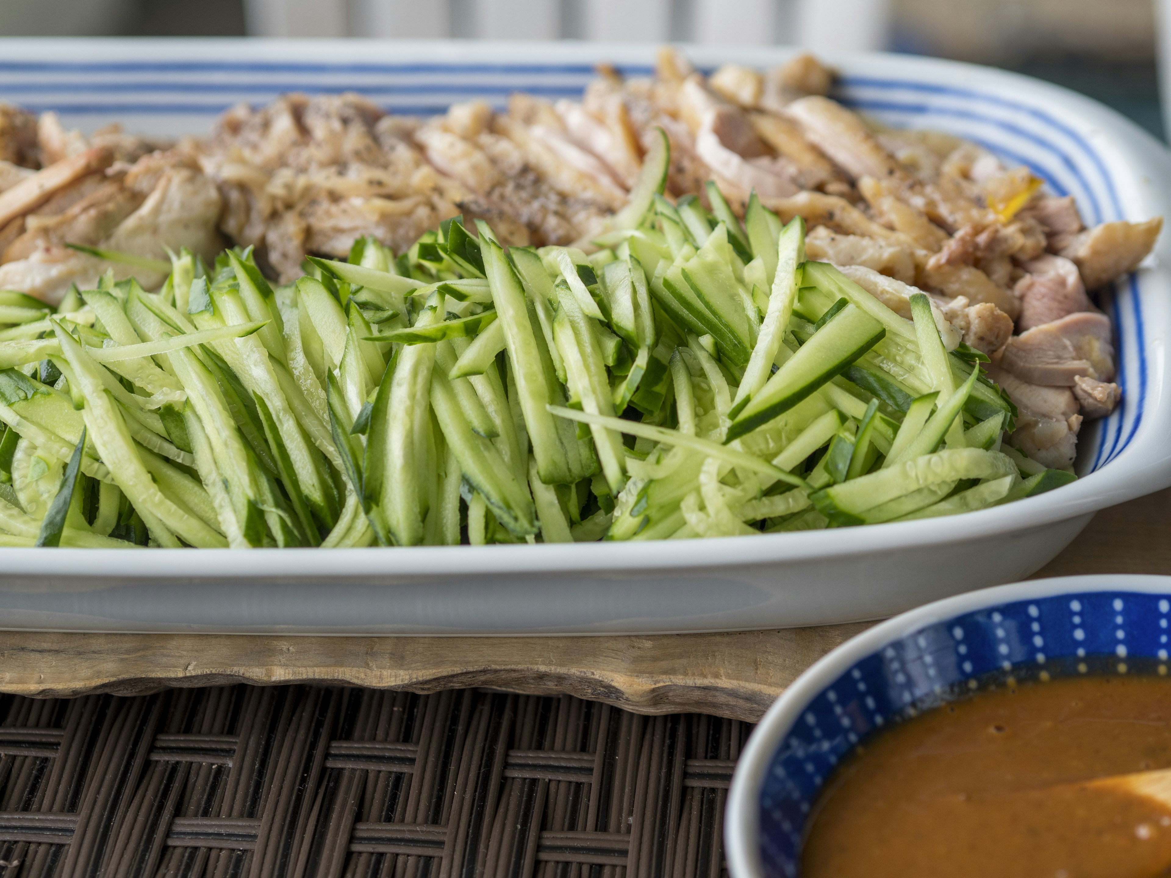 Sliced cucumbers and chicken on a platter with peanut sauce