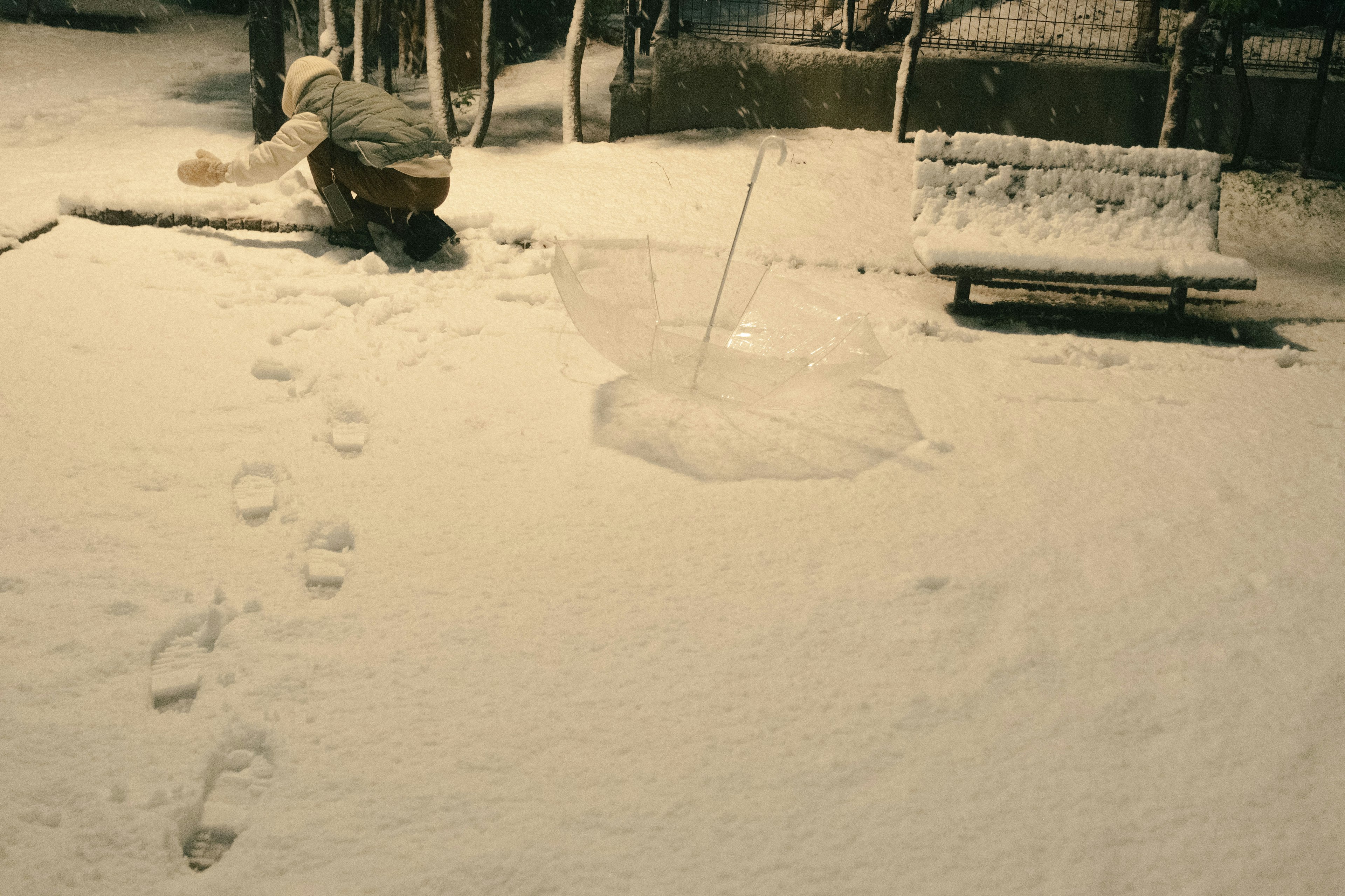 A person using an umbrella in the snow with footprints in a park