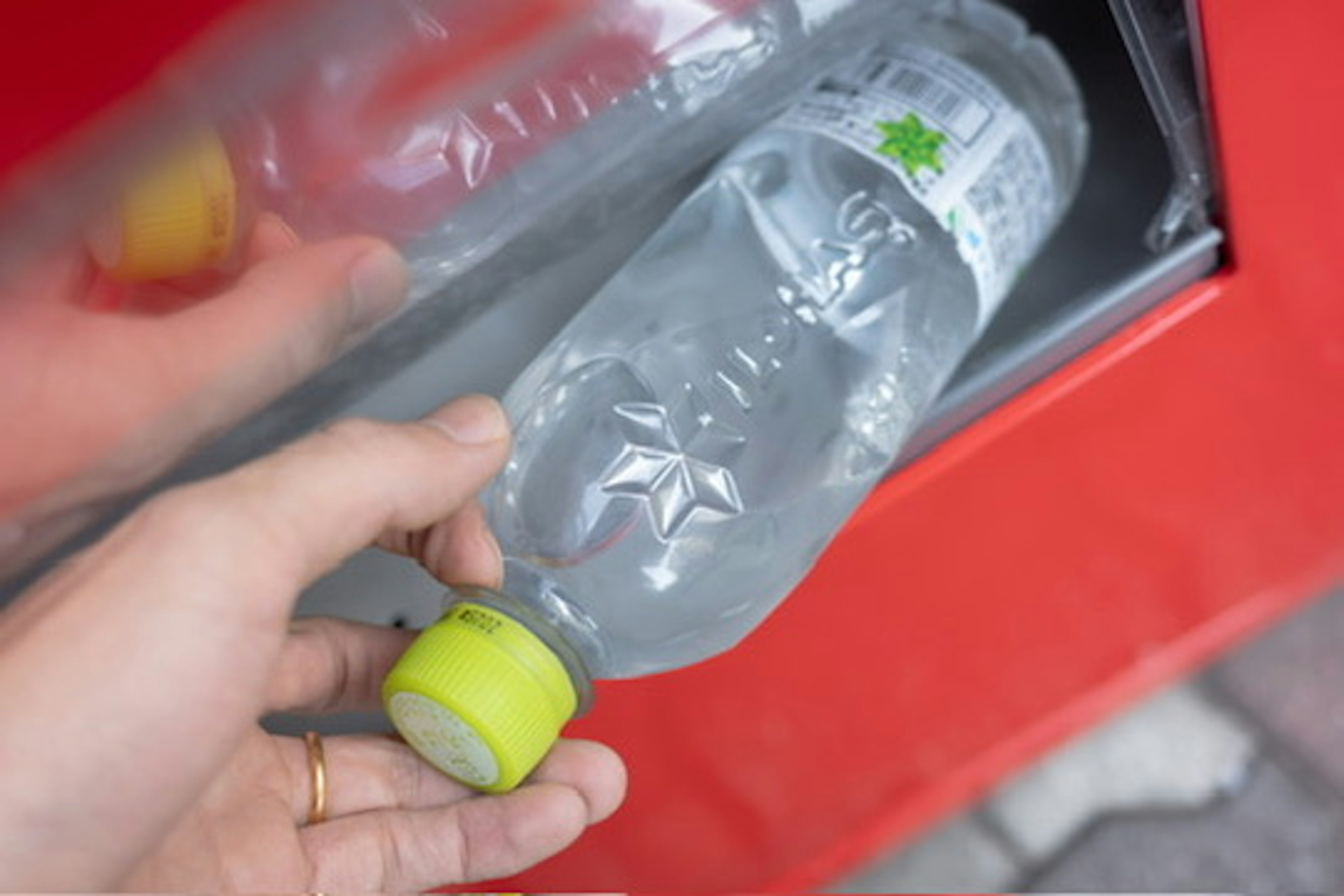 Tangan meletakkan botol air ke dalam tempat daur ulang merah