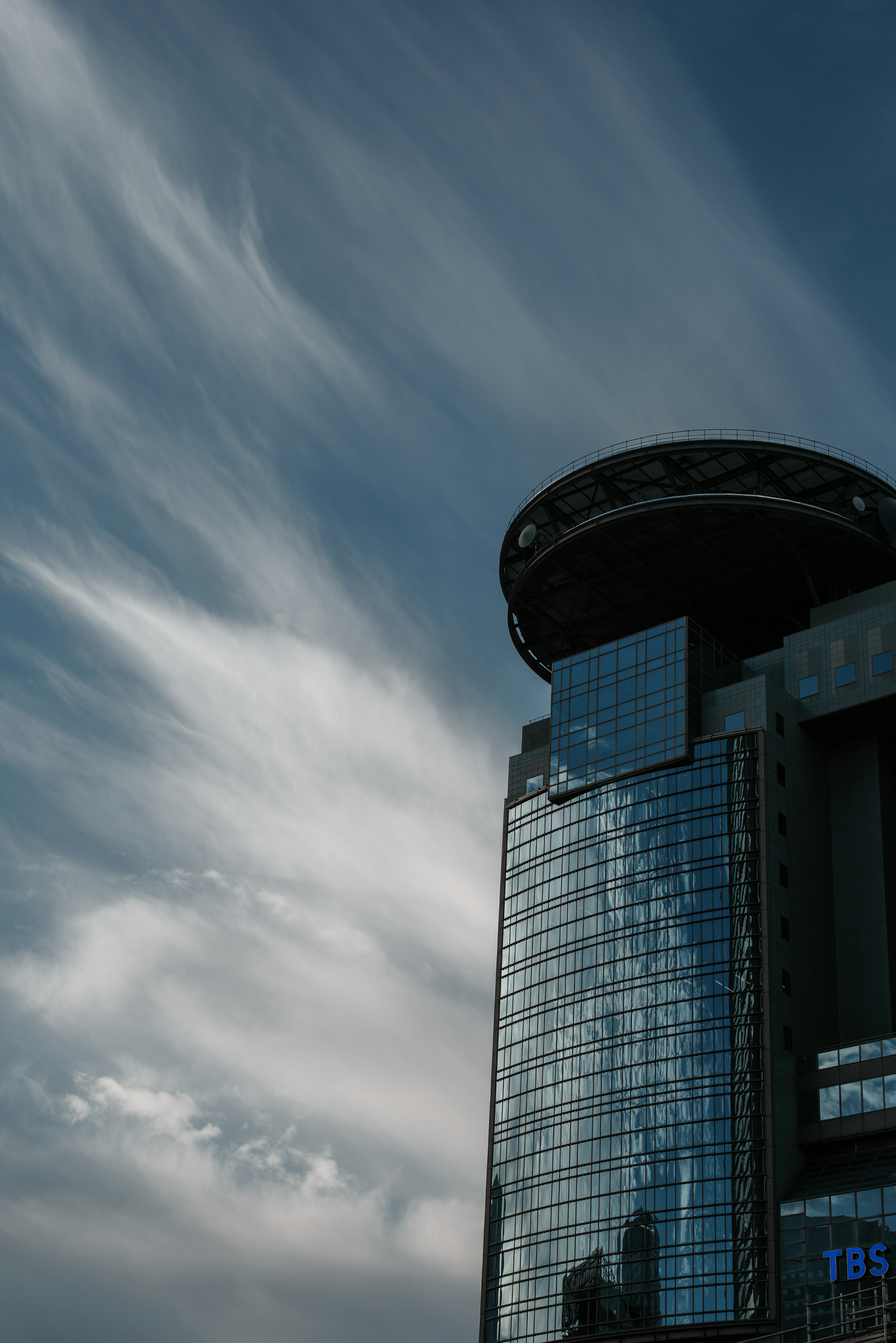 Tampilan samping gedung pencakar langit dengan fasad kaca dan desain atap yang unik