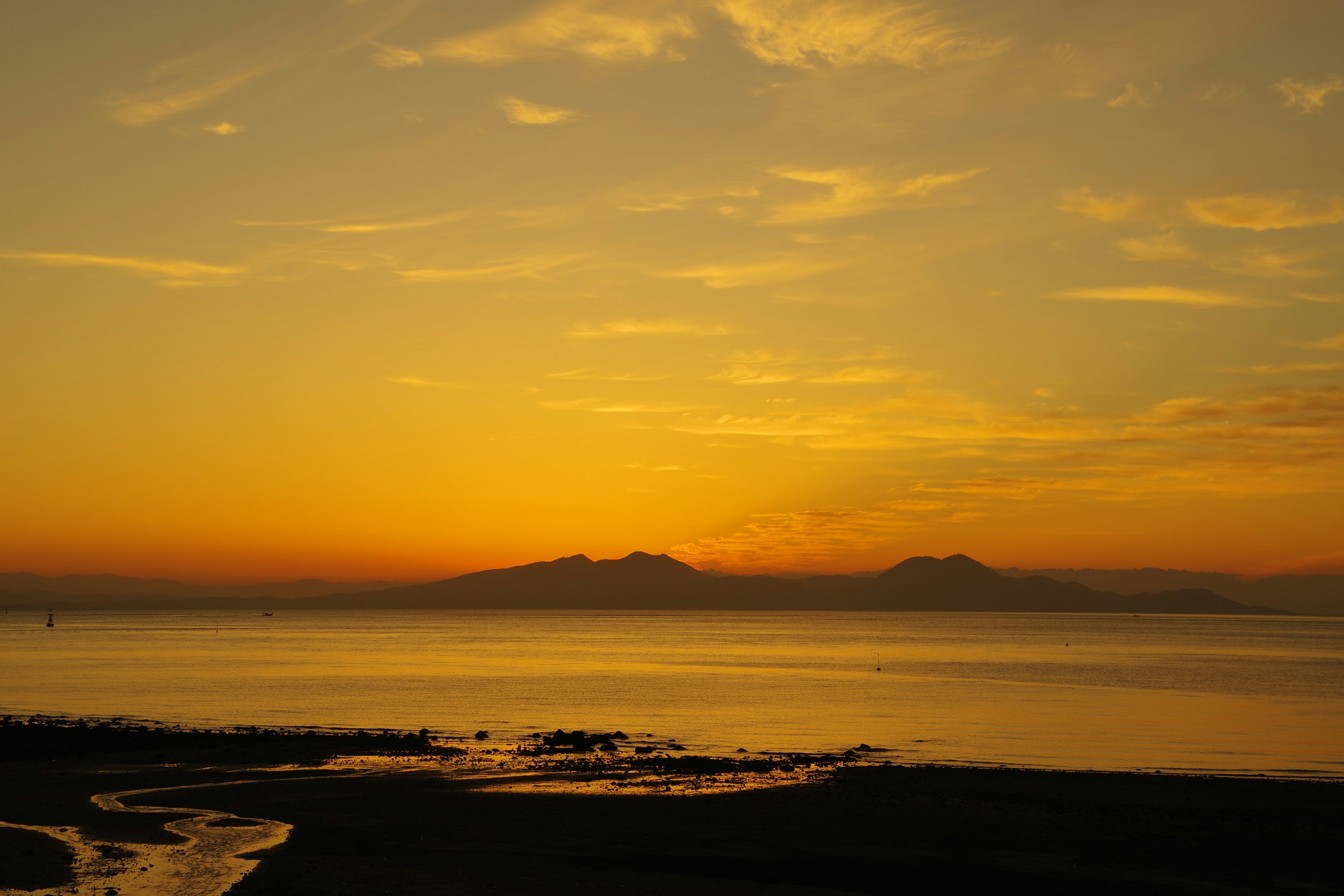 Langit senja di atas laut tenang dengan gunung siluet