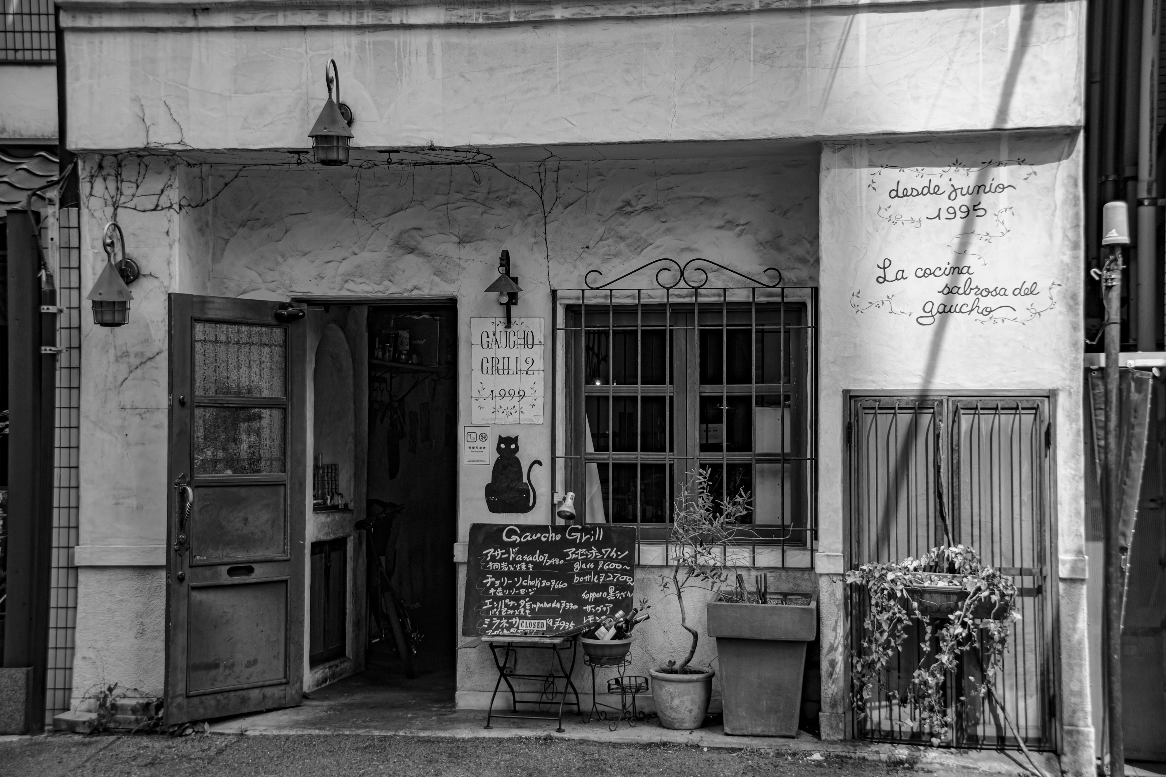 Small building with a black and white exterior featuring an iron door and distinctive windows a chalkboard menu displayed