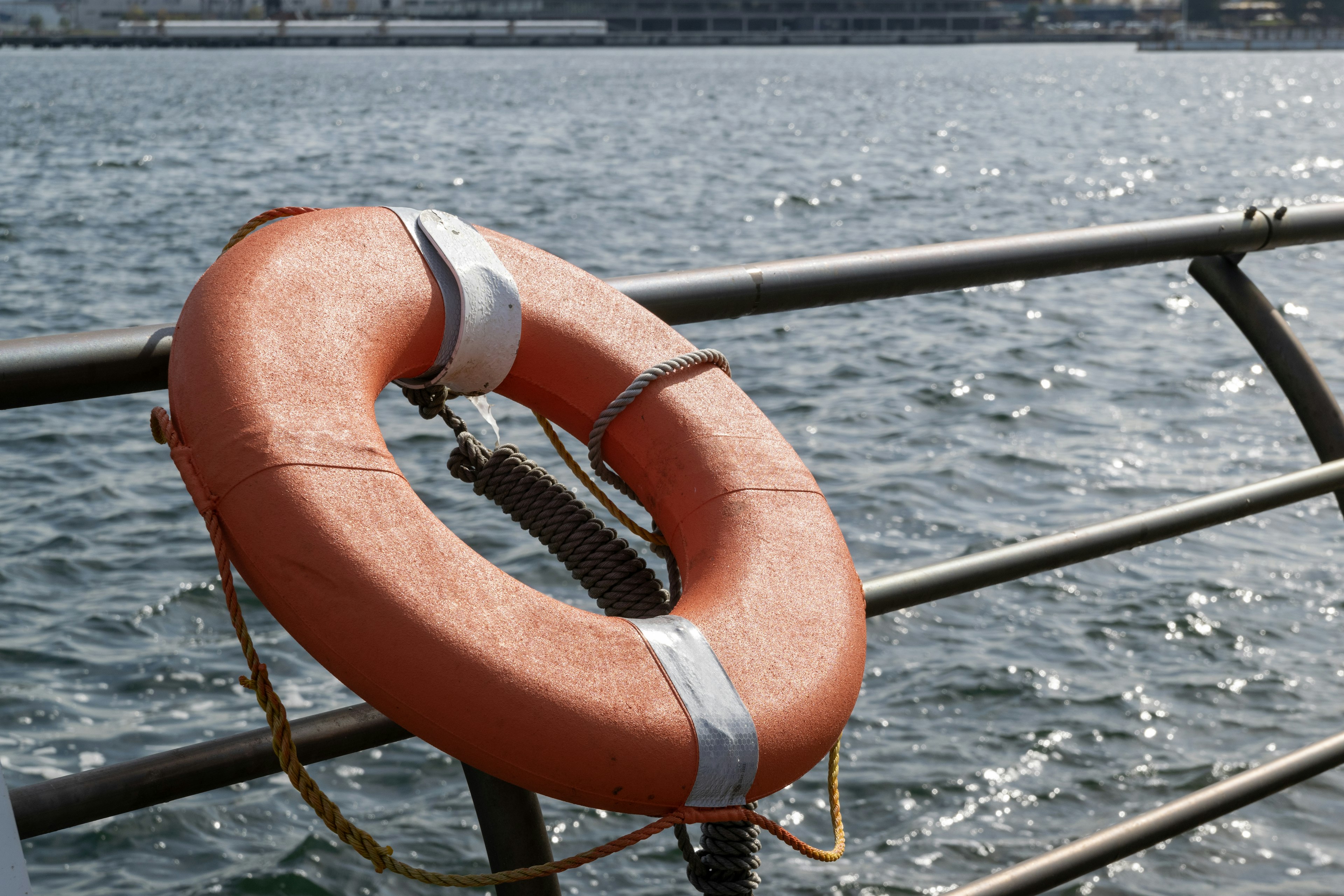 An orange life buoy hanging on a boat railing near the water