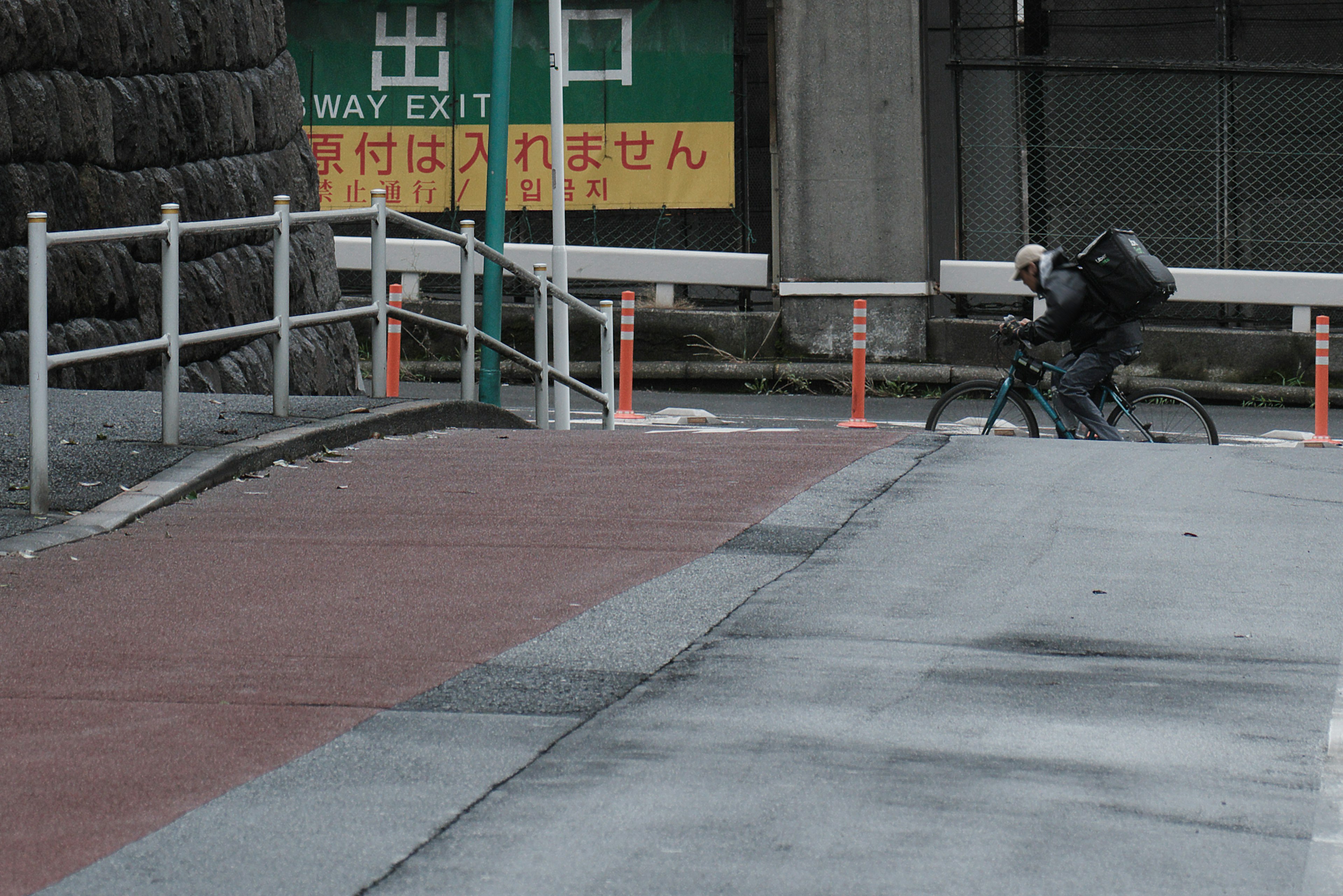 Bicycle courier on a sloped pathway with a green exit sign