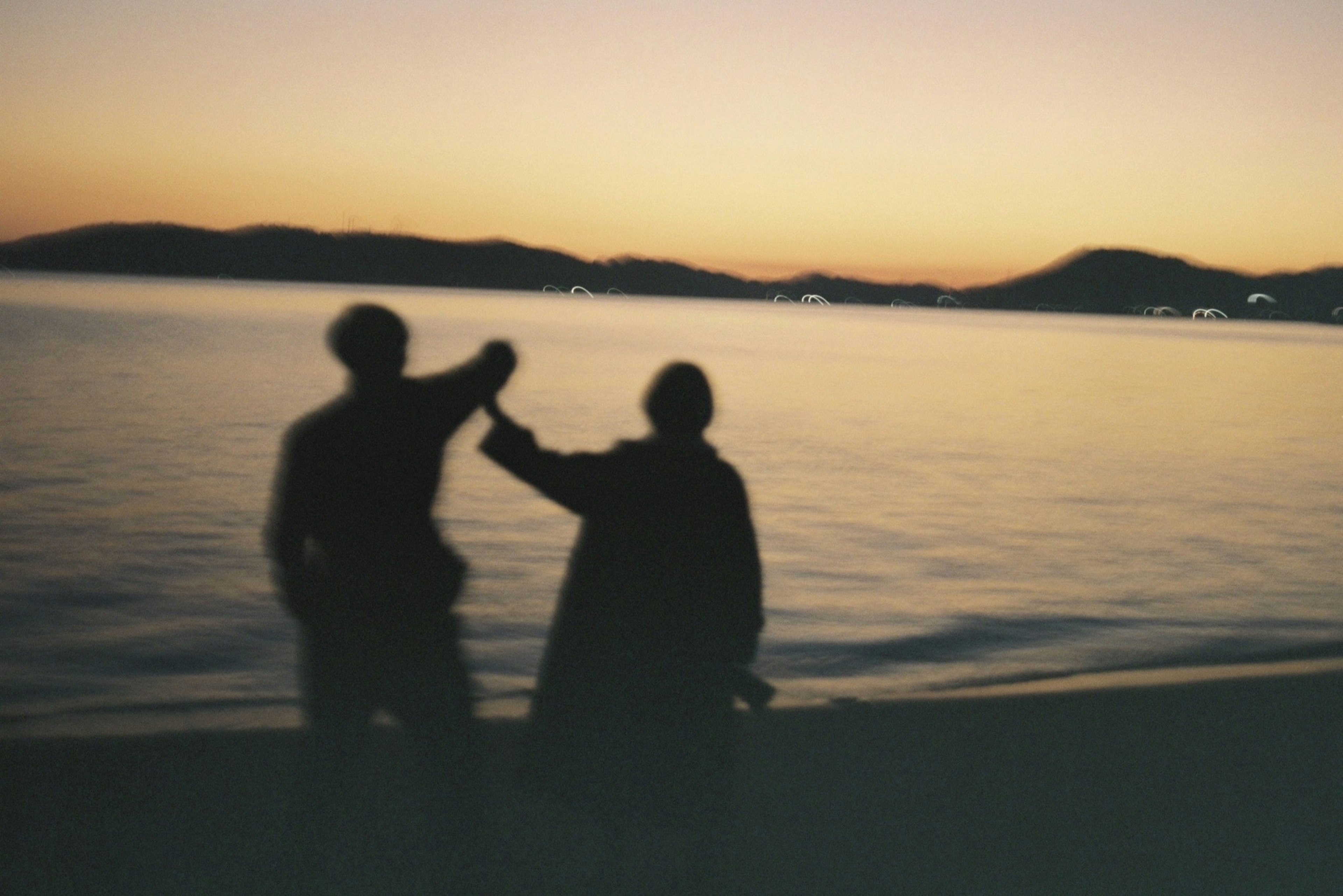 Silhouette von zwei Personen, die sich bei Dämmerung am Meer die Hände halten