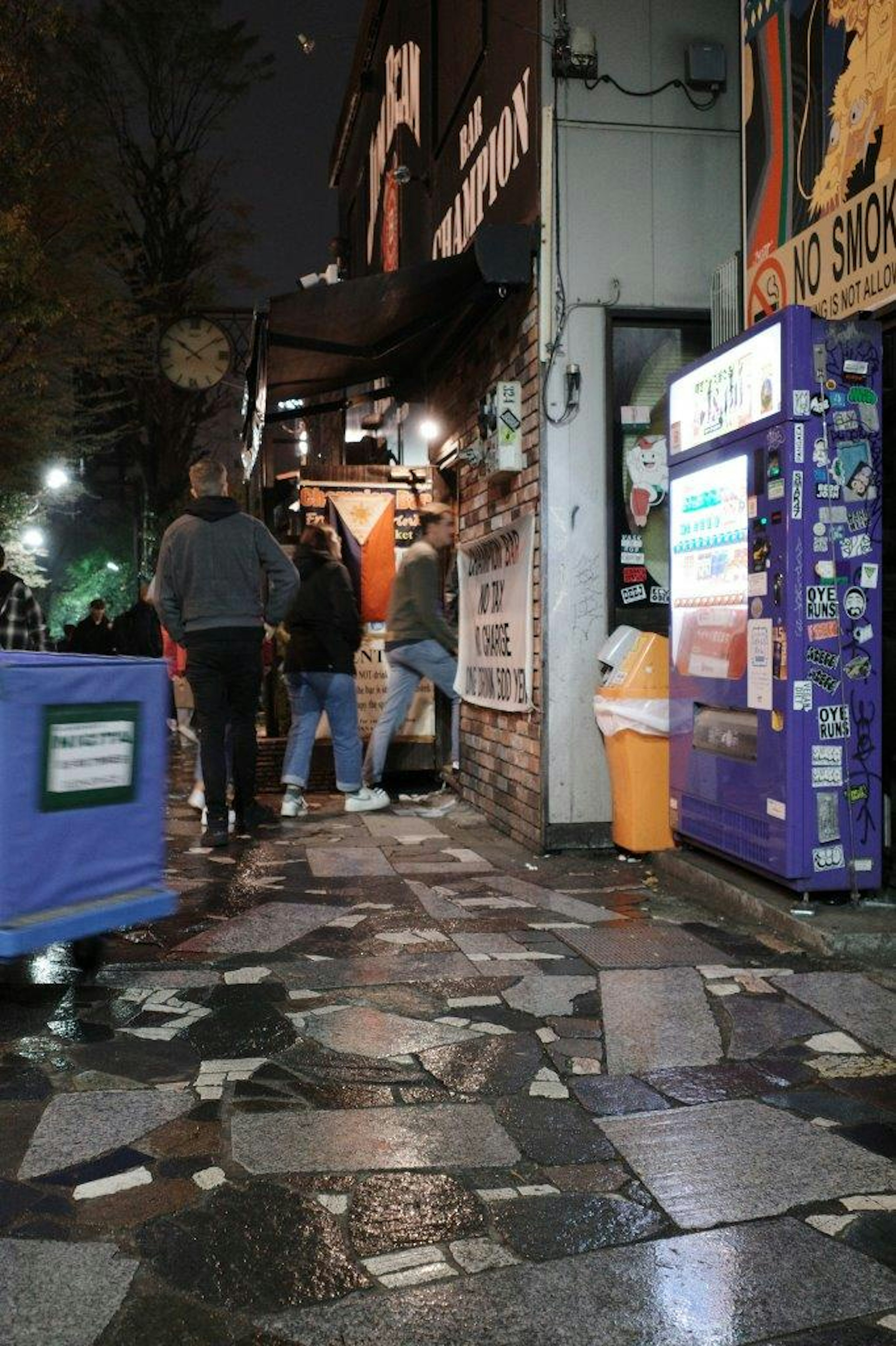 Angolo di strada di notte con negozi e persone su un marciapiede piastrellato