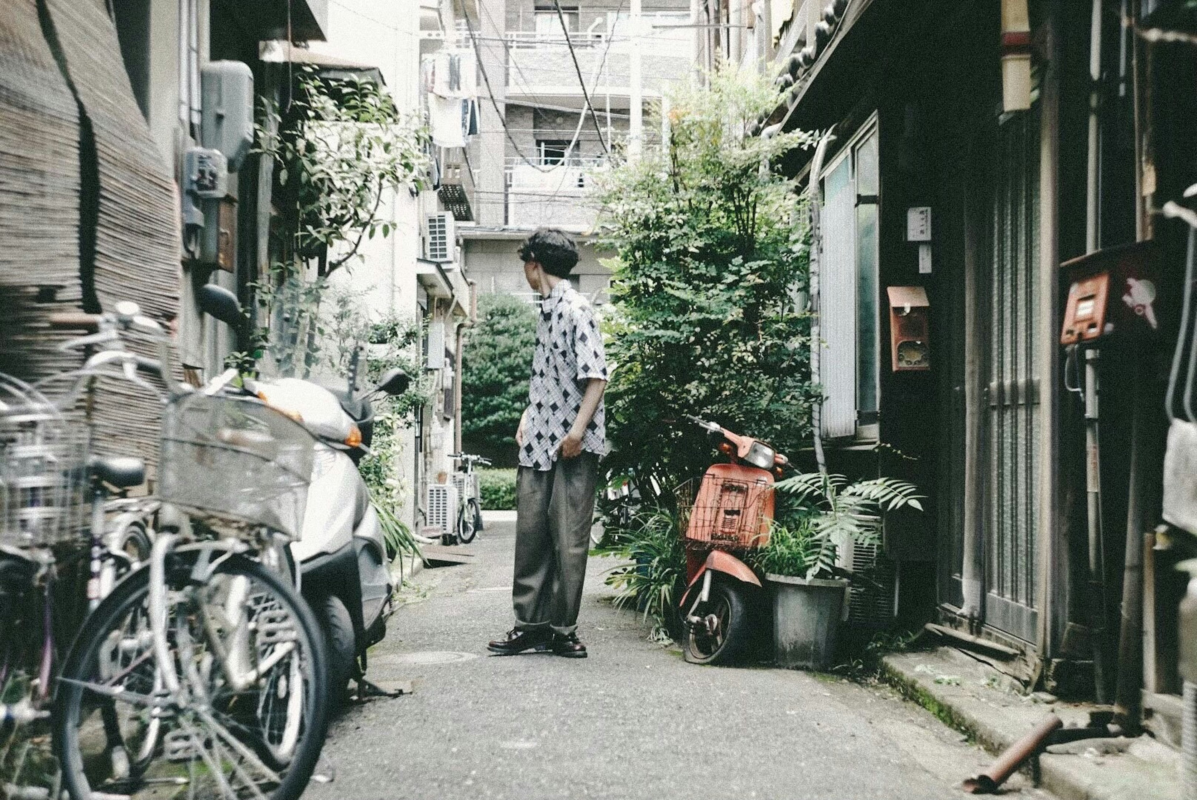 Un homme se tenant dans une ruelle étroite avec des vélos et un scooter