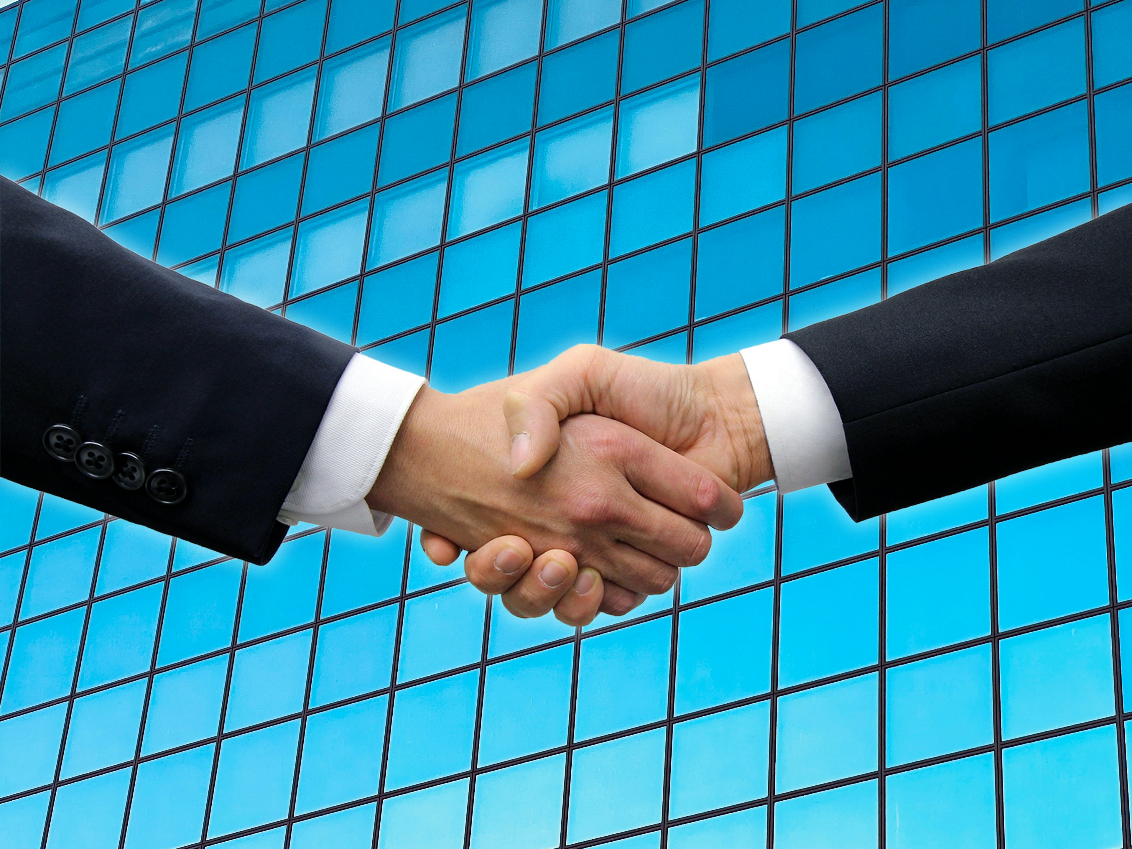 Businessmen shaking hands in front of a blue glass building