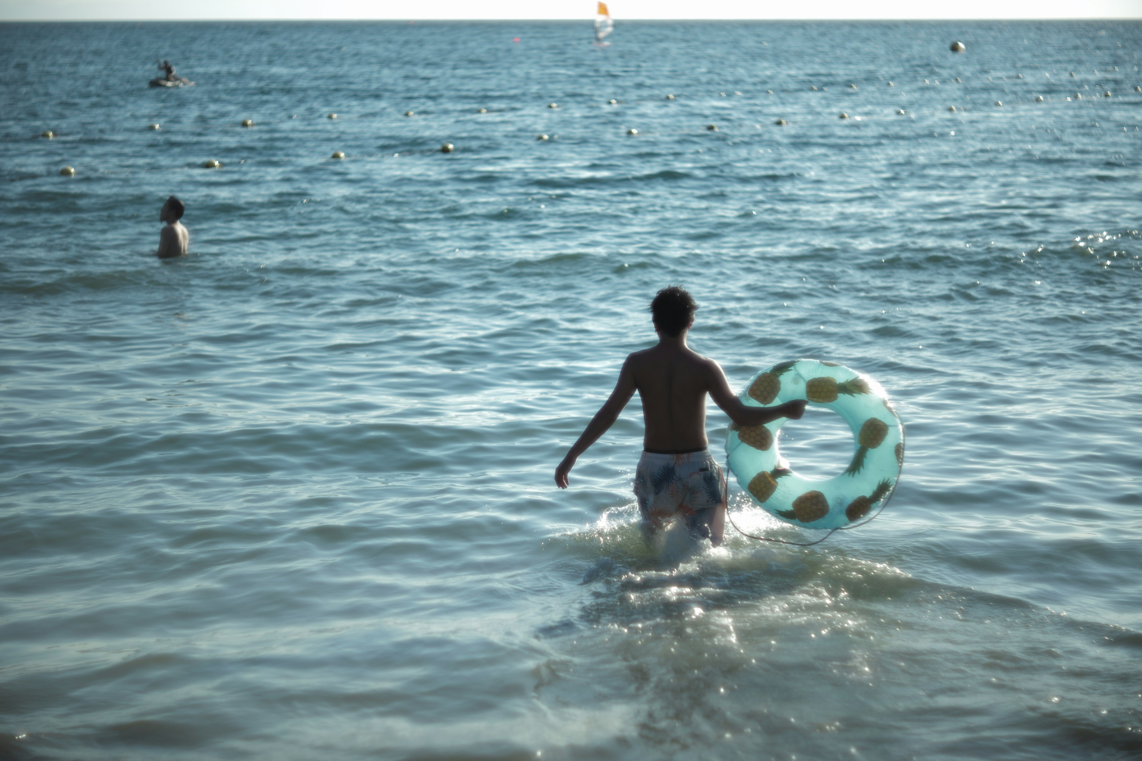 A boy holding a float in the sea walking away