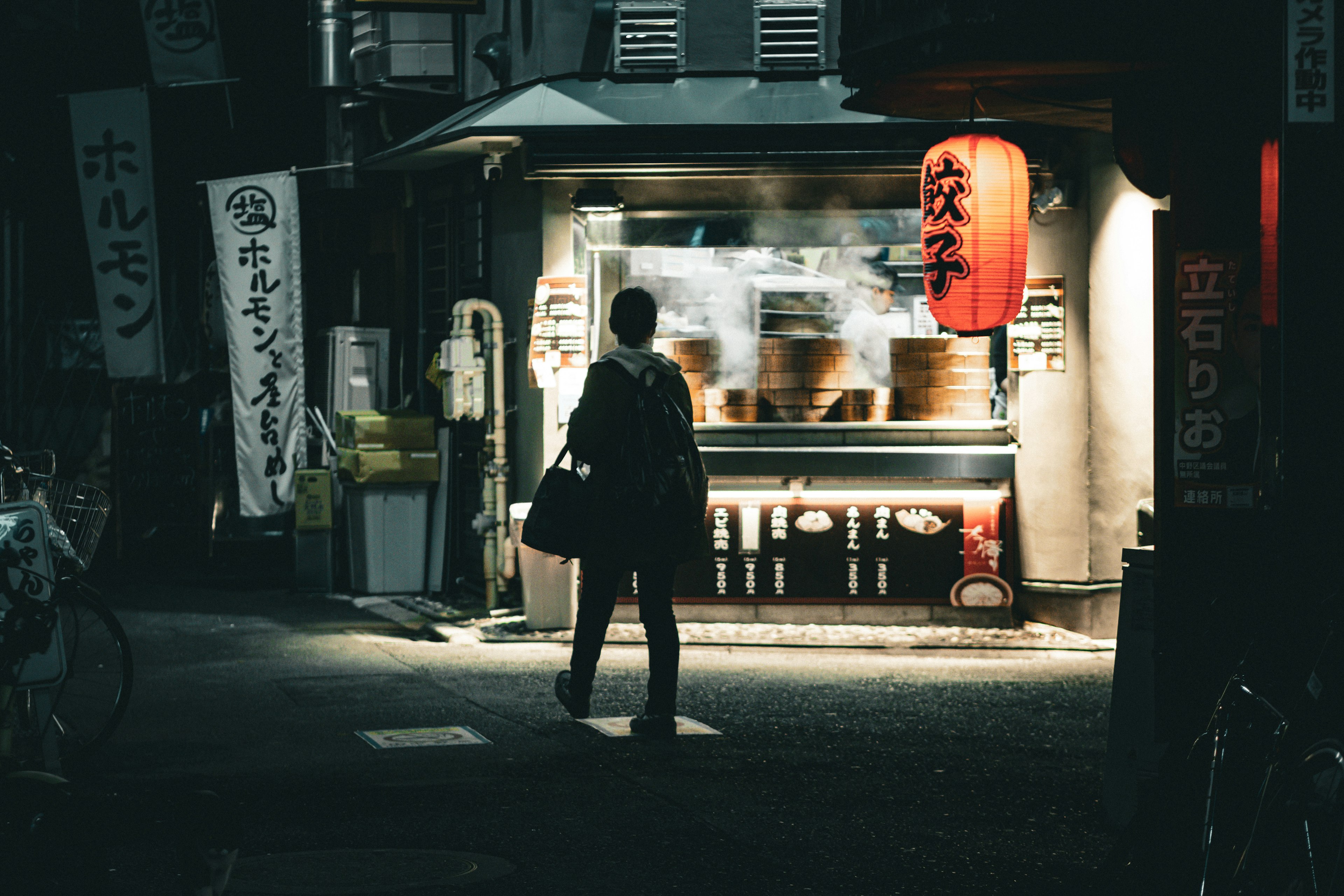 Street vendor at night featuring steaming ramen and lantern