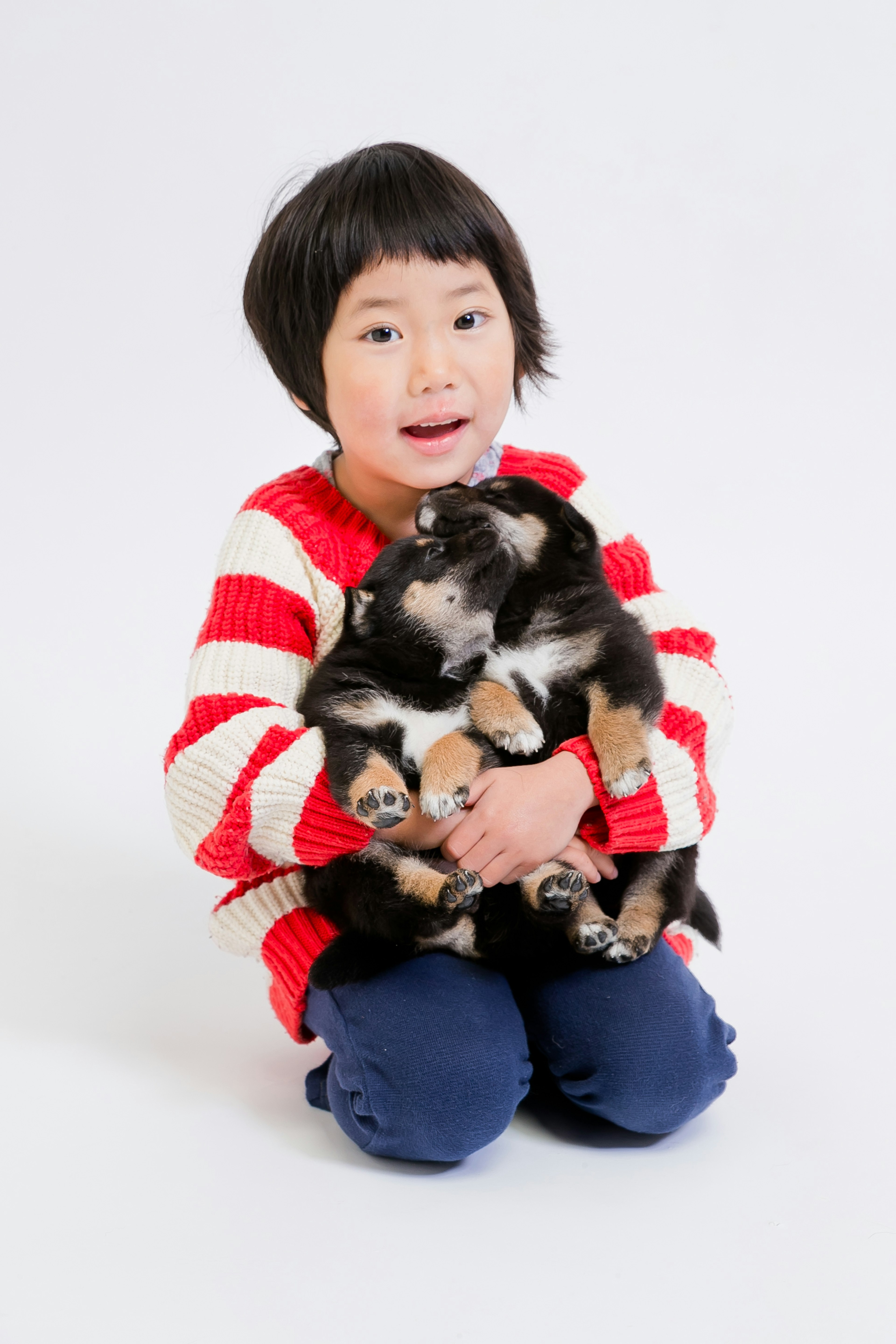 Child in red striped sweater holding black puppies