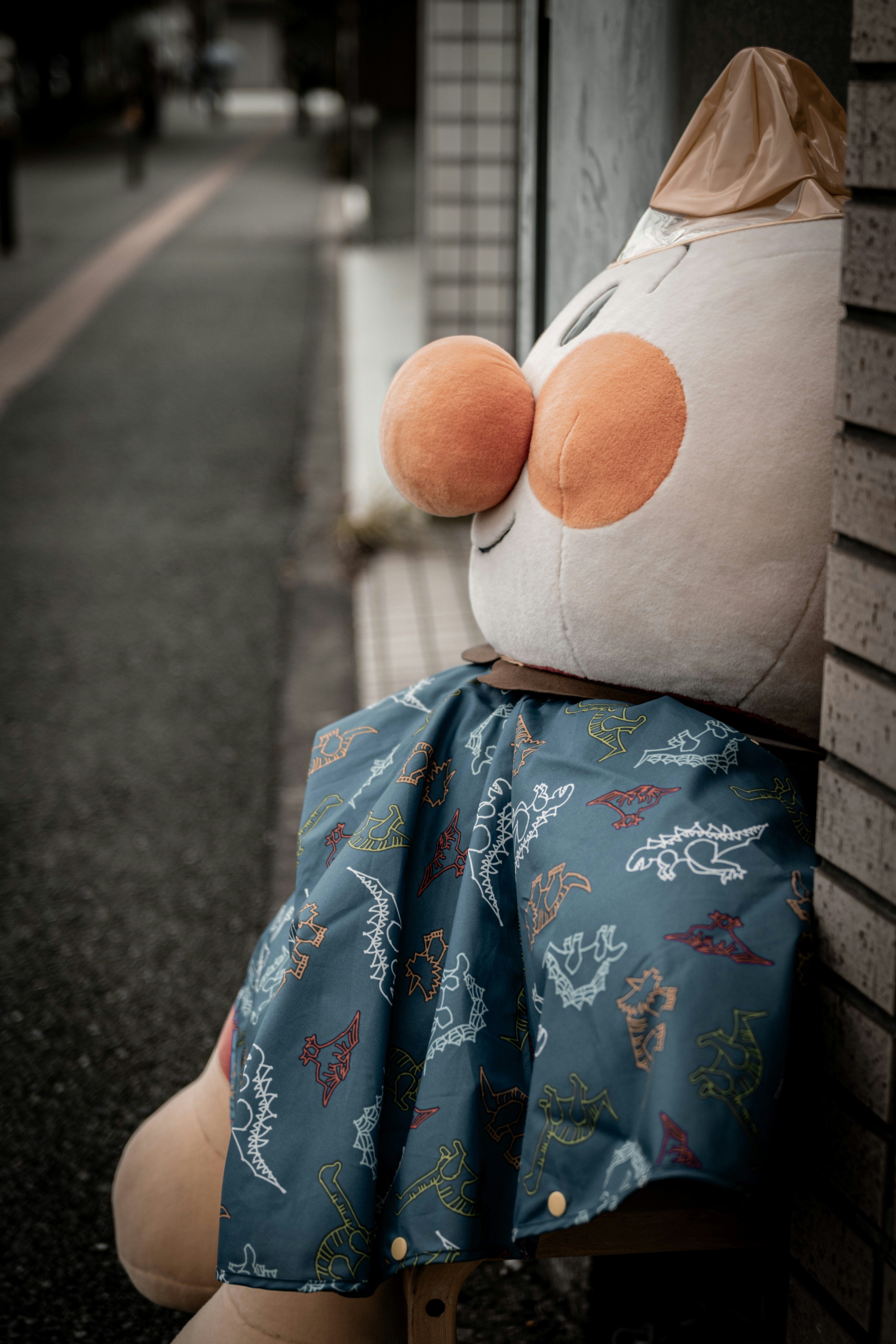 A cute doll sitting on the corner wearing a blue skirt