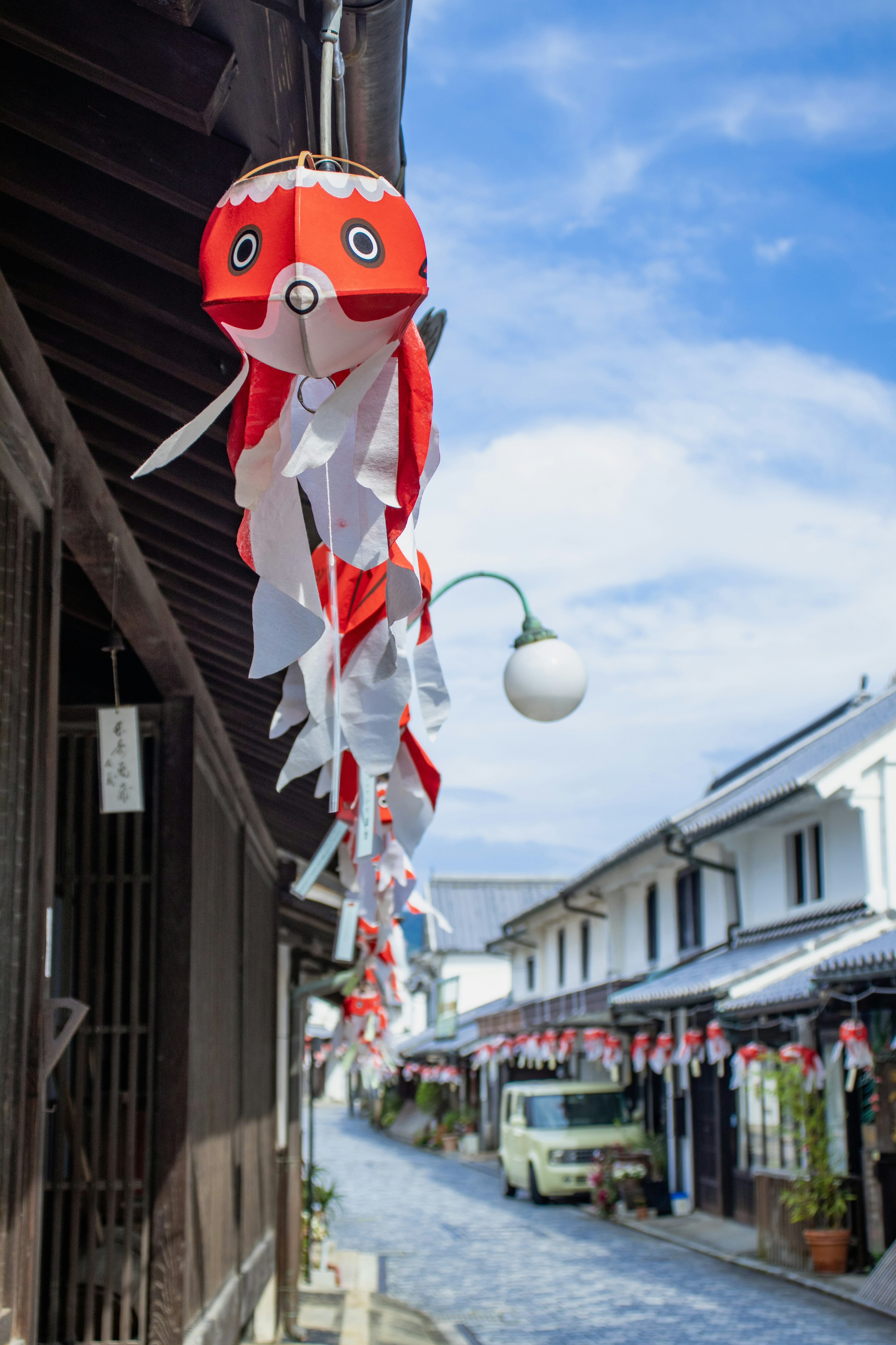 Vista de una calle con una decoración de koi nobori rojo y casas tradicionales