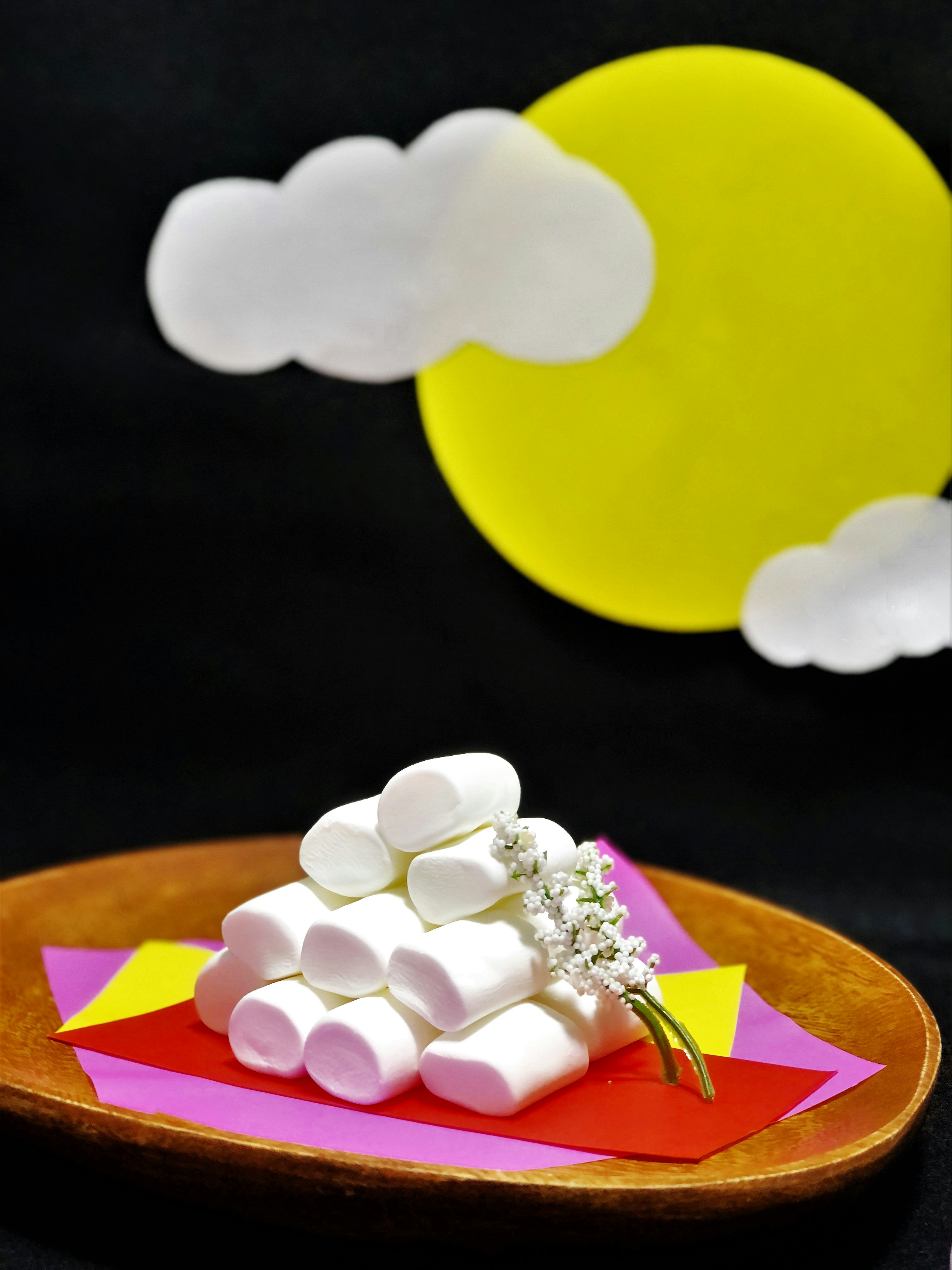 Piring dengan marshmallow putih yang ditumpuk dan matahari kuning dengan awan putih di latar belakang