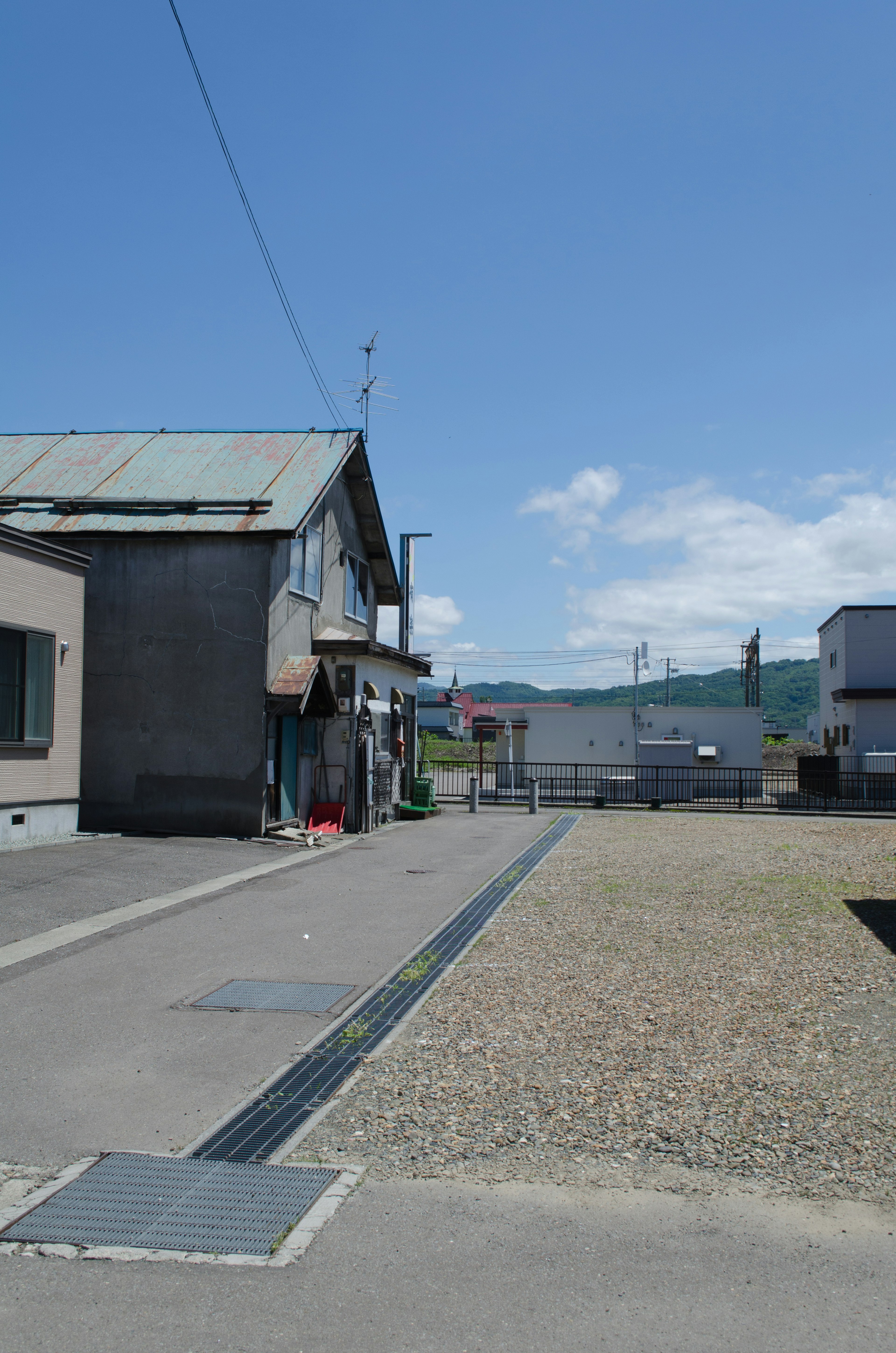 Scena di una strada residenziale sotto un cielo blu con un vecchio edificio e una strada pavimentata