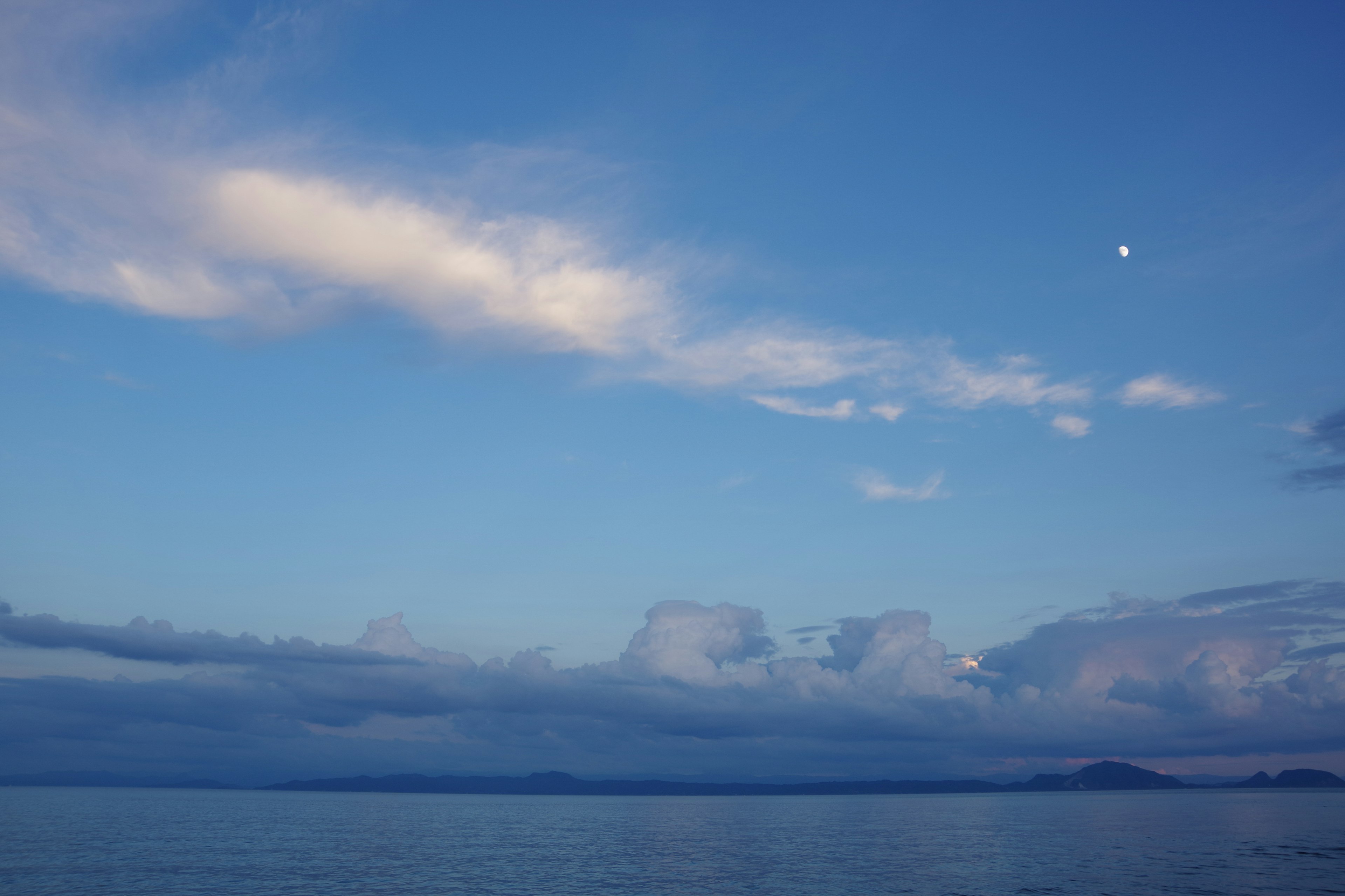 青い空と雲の風景に浮かぶ月