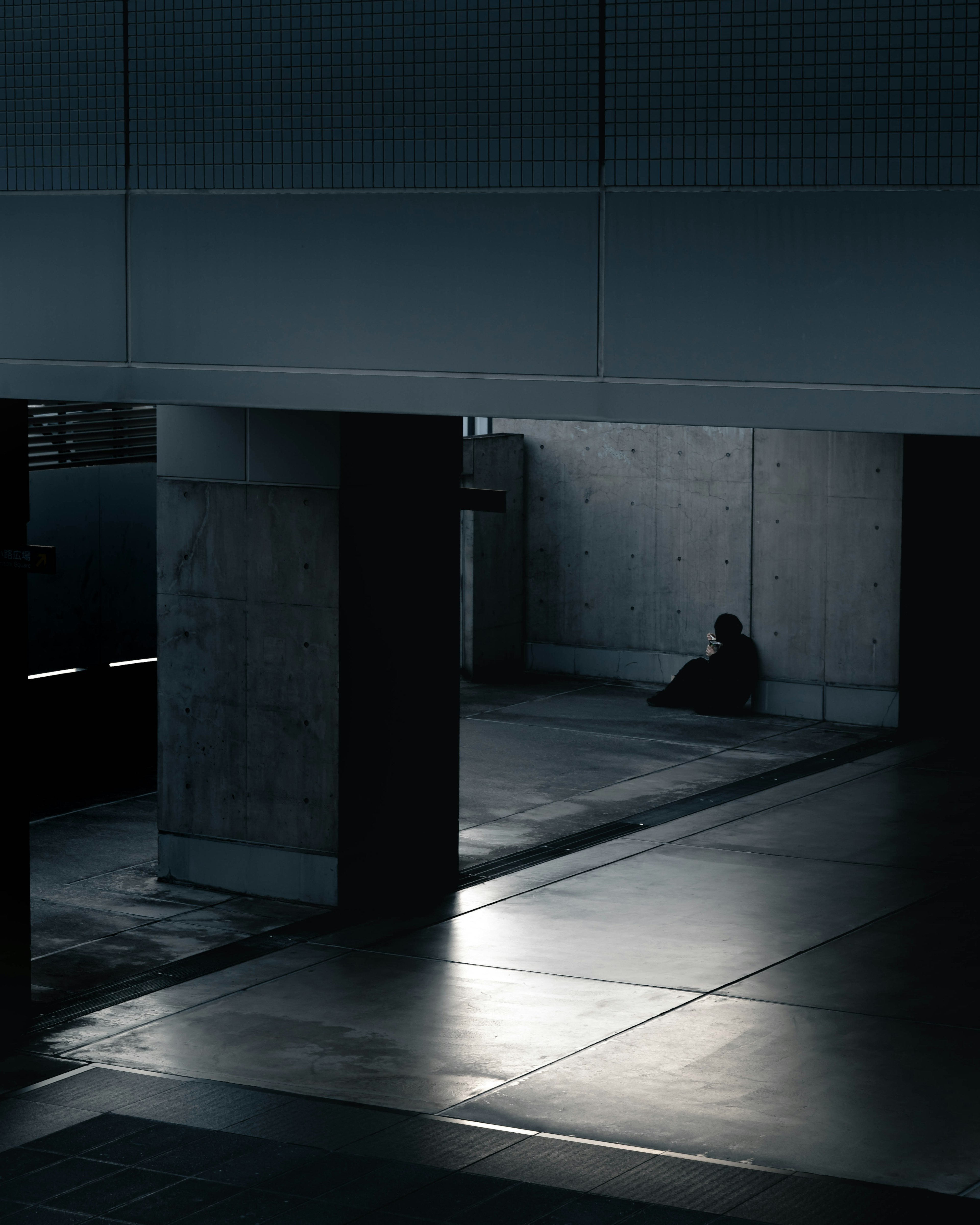 Personne assise dans un cadre urbain sombre entre des piliers en béton