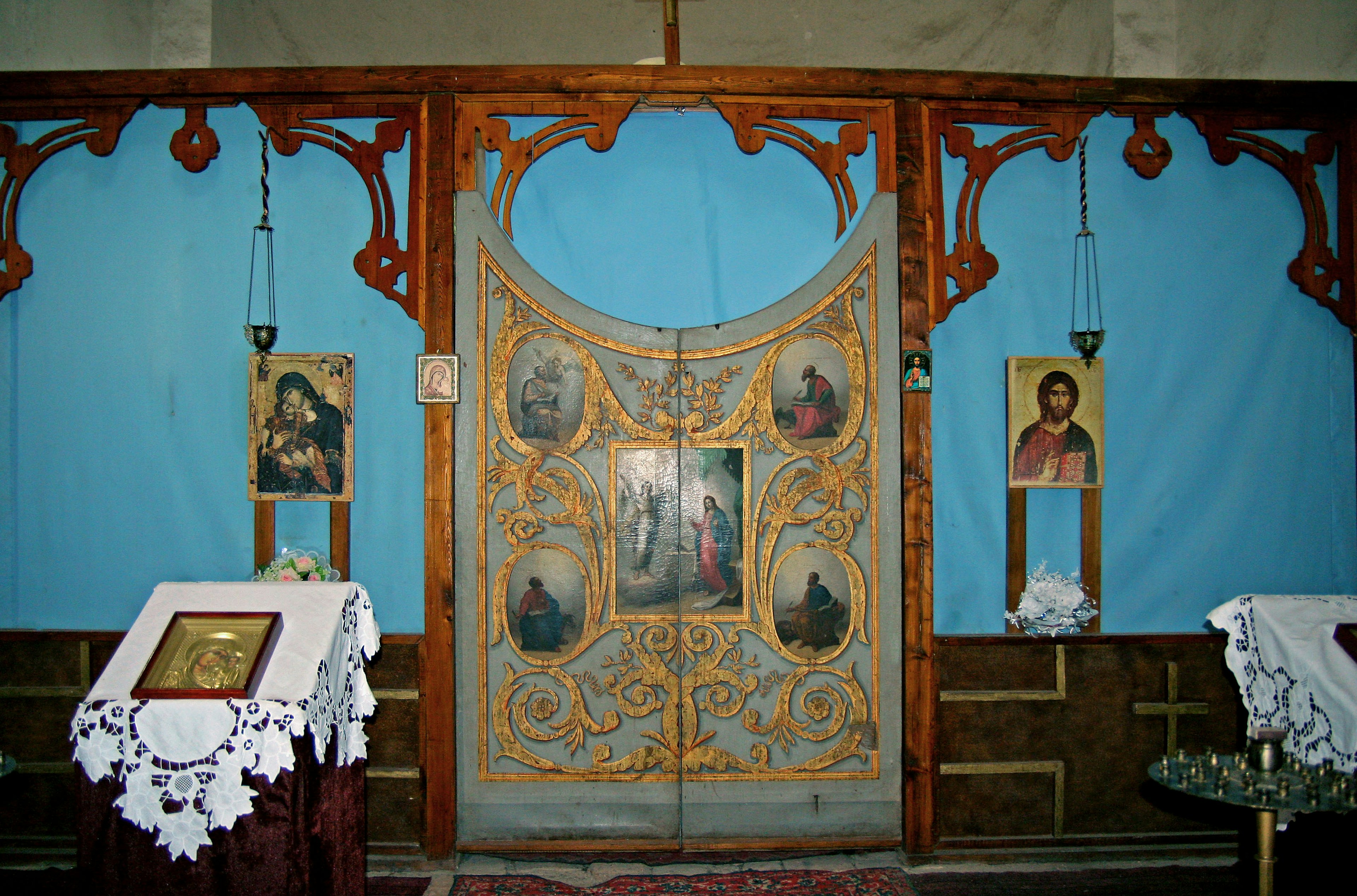 Innenansicht einer Kirche mit dekorativen Holztüren und Ikonen vor einem blauen Stoffhintergrund