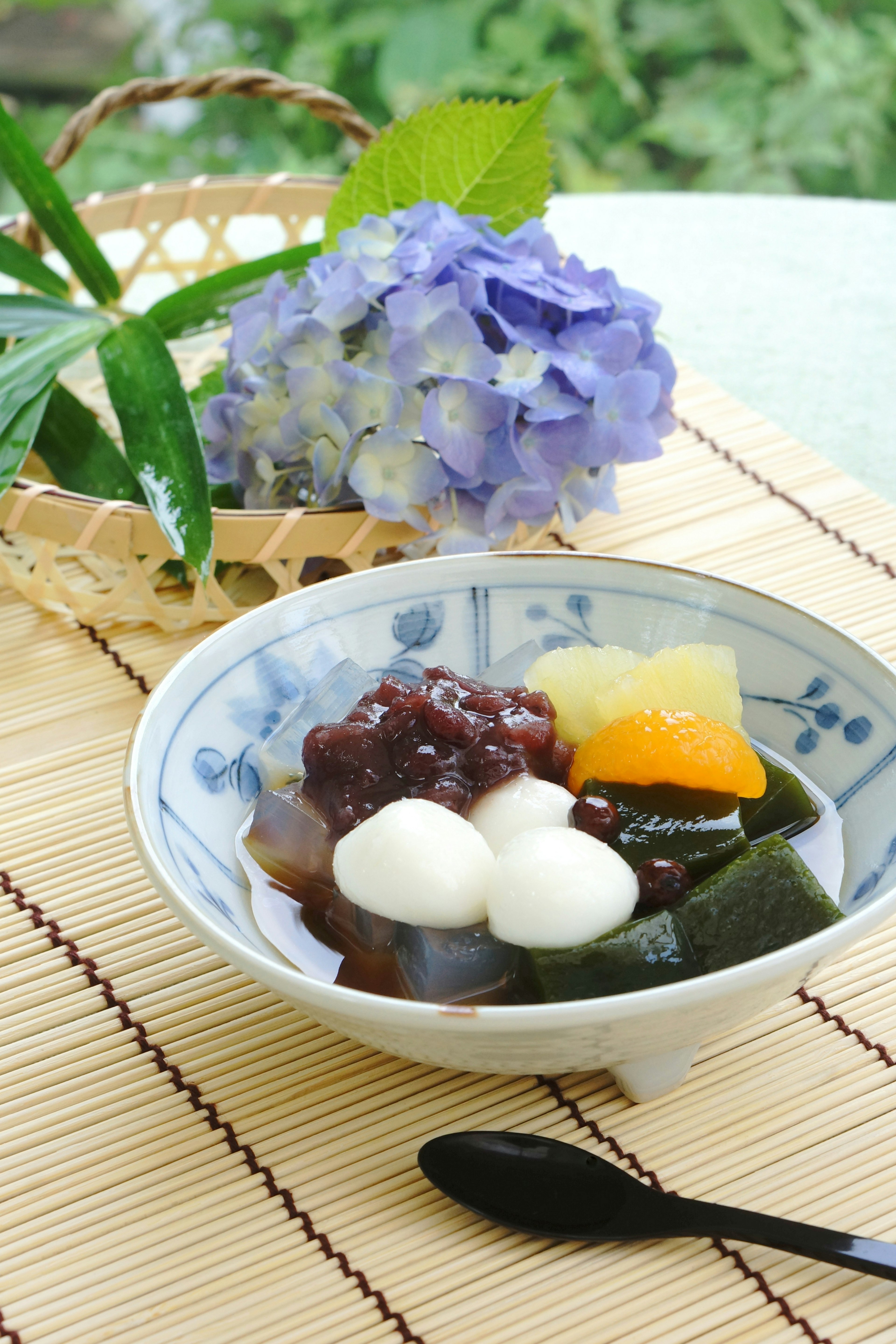 Mangkuk dessert Jepang dengan bola nasi dan pasta kacang merah manis dengan bunga hydrangea di latar belakang