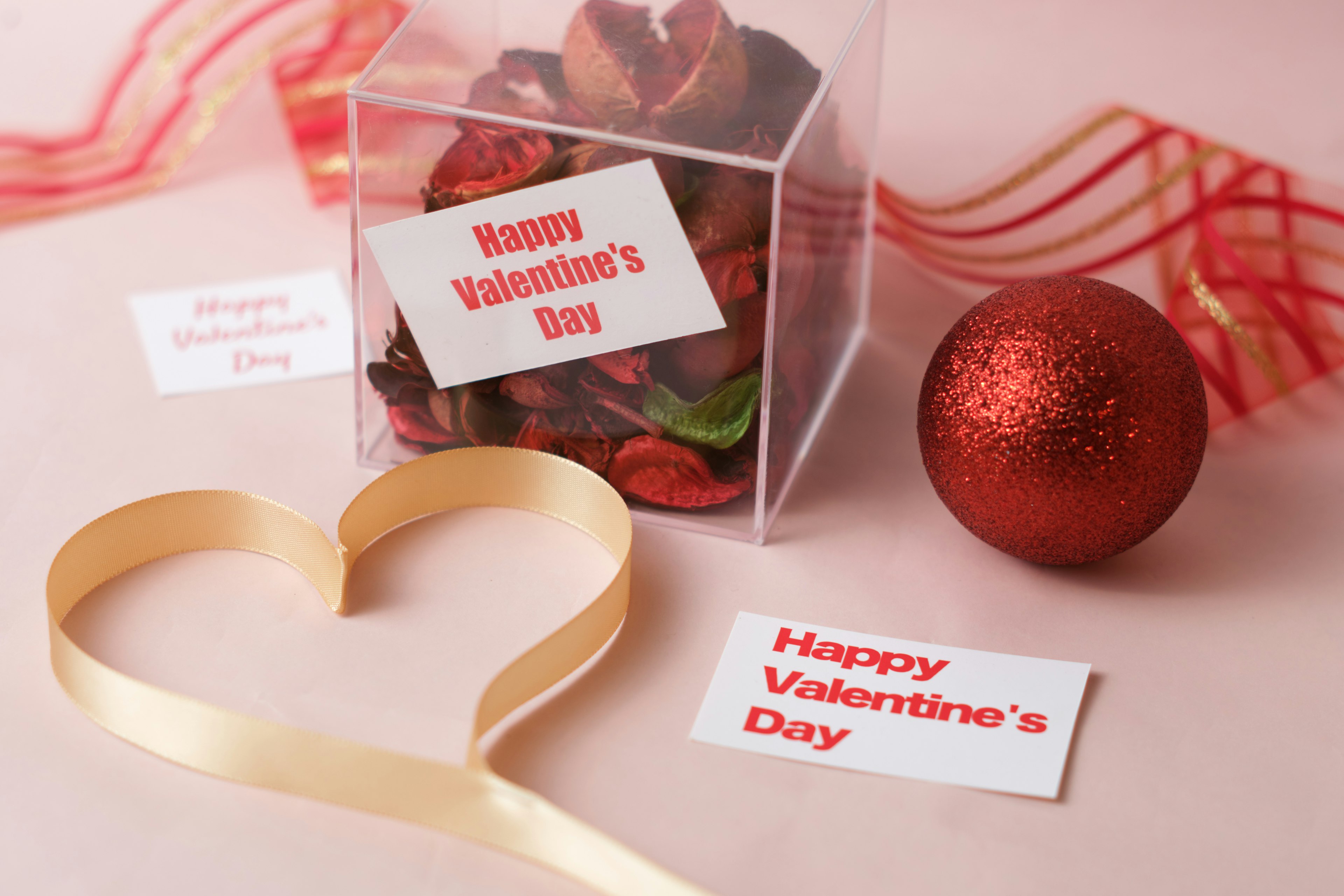 Decoraciones del Día de San Valentín que incluyen una caja transparente con potpourri una bola roja y un corazón de cinta