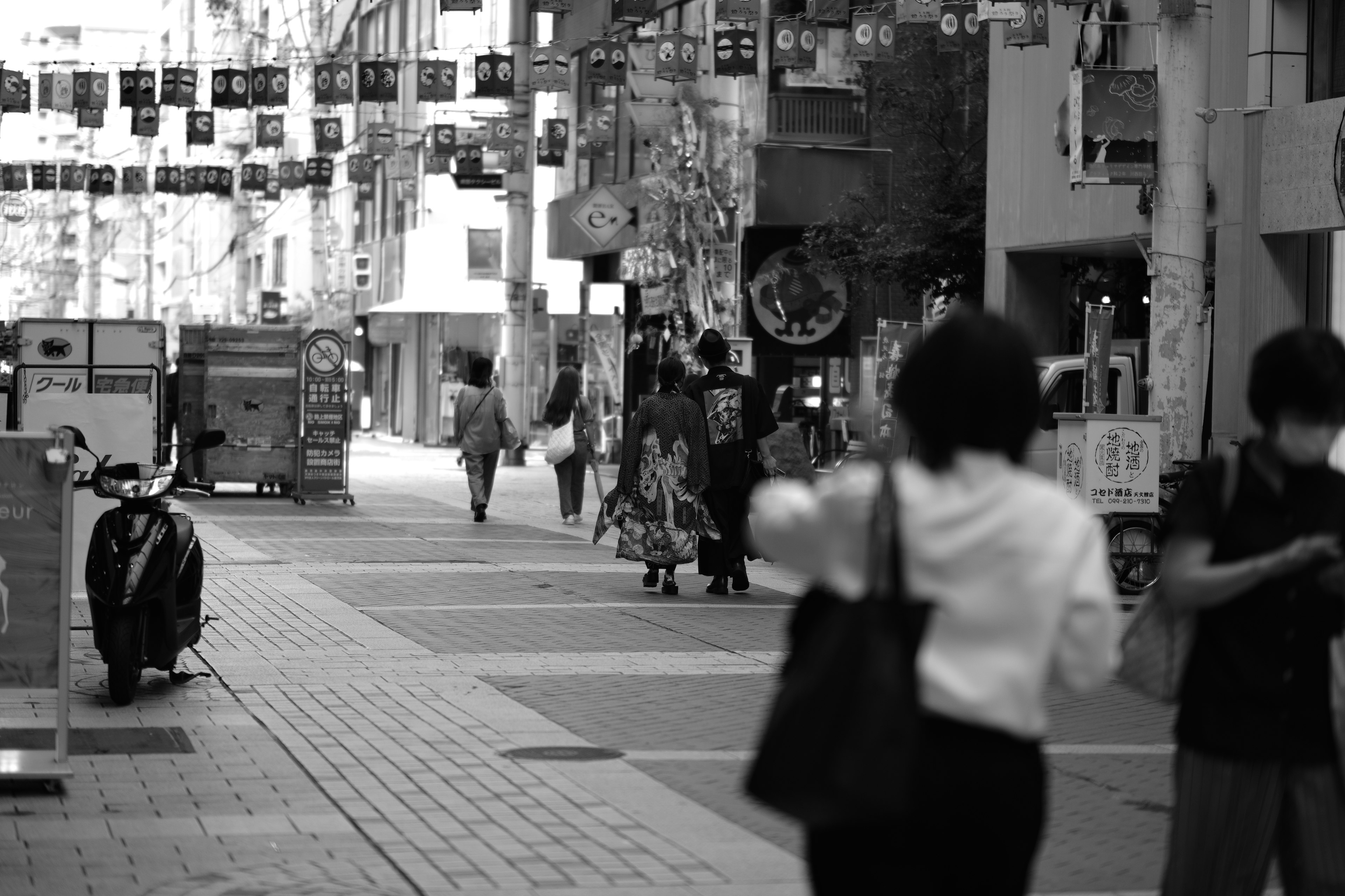 Black and white street scene with people walking and various signs