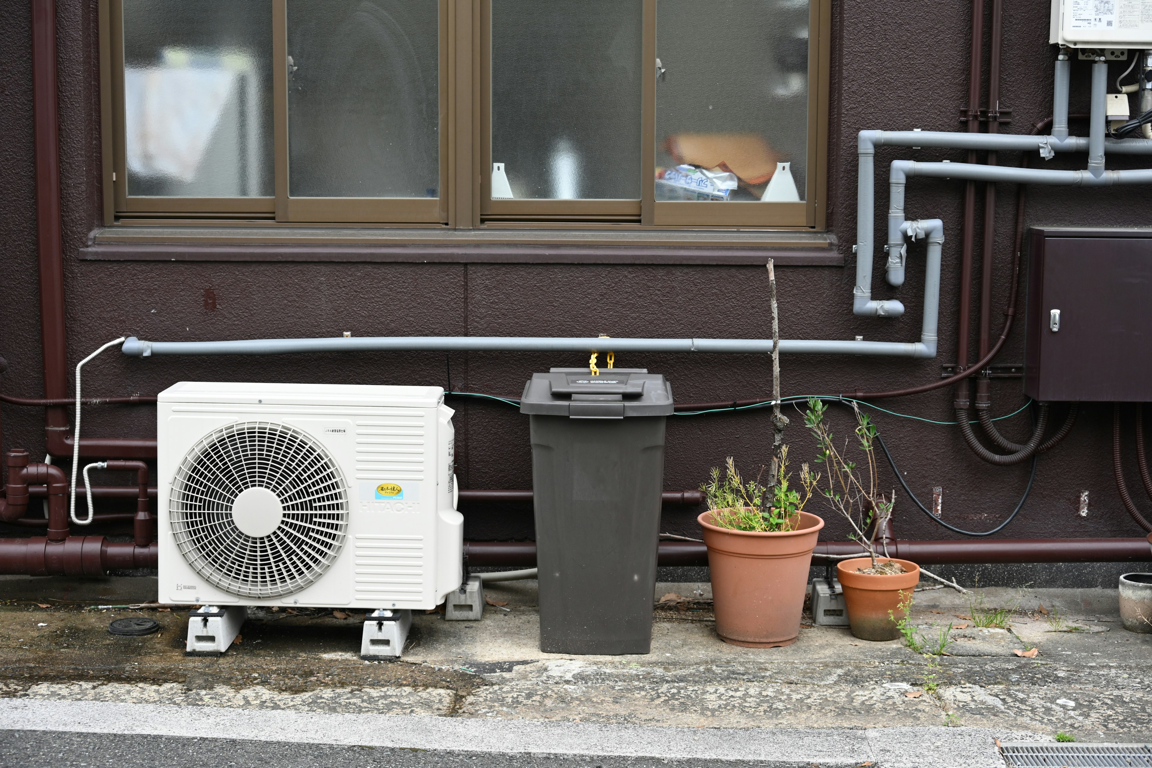 Air conditioner next to a trash bin and potted plants by a building