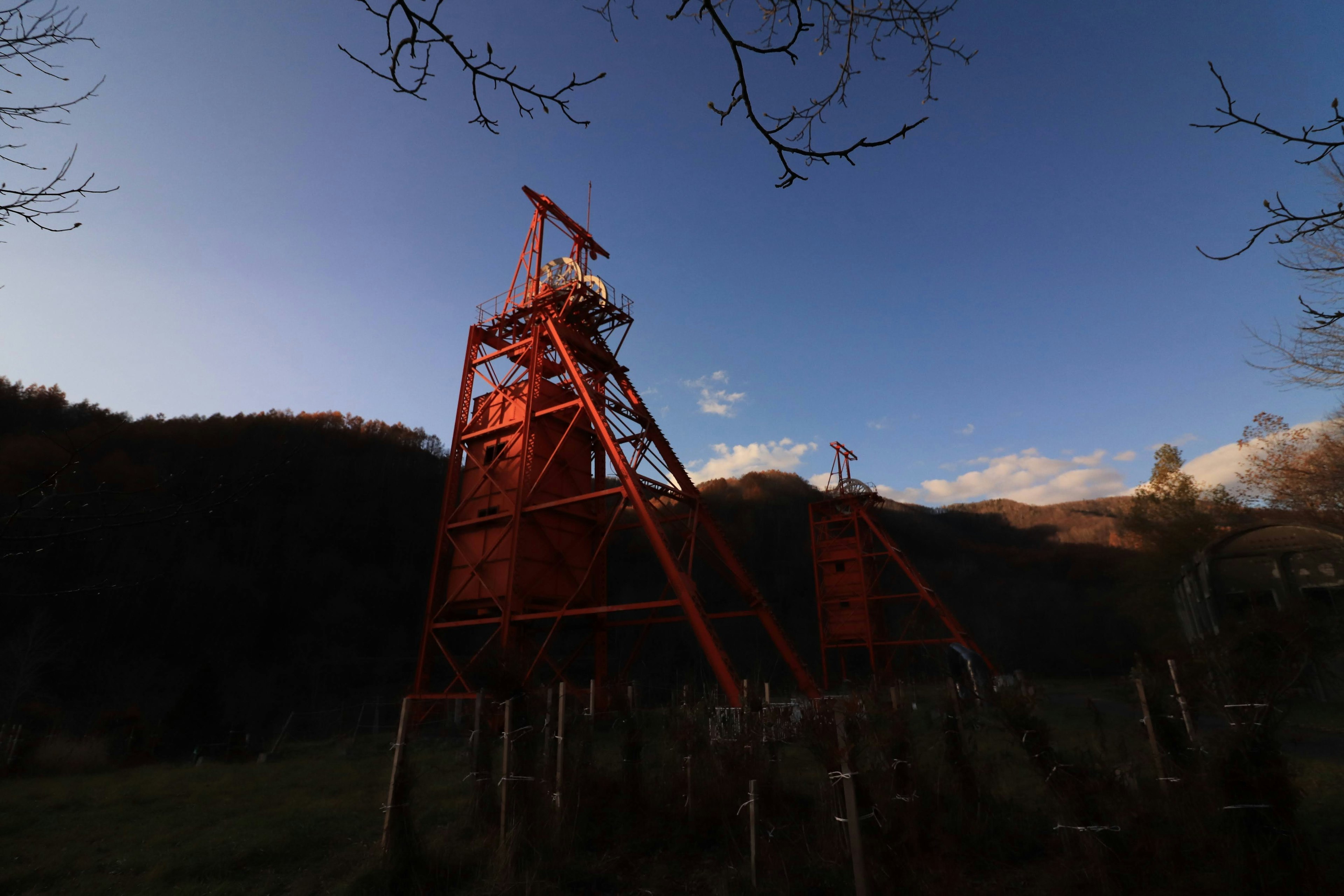 Red oil well tower silhouetted against a dusk sky with mountains