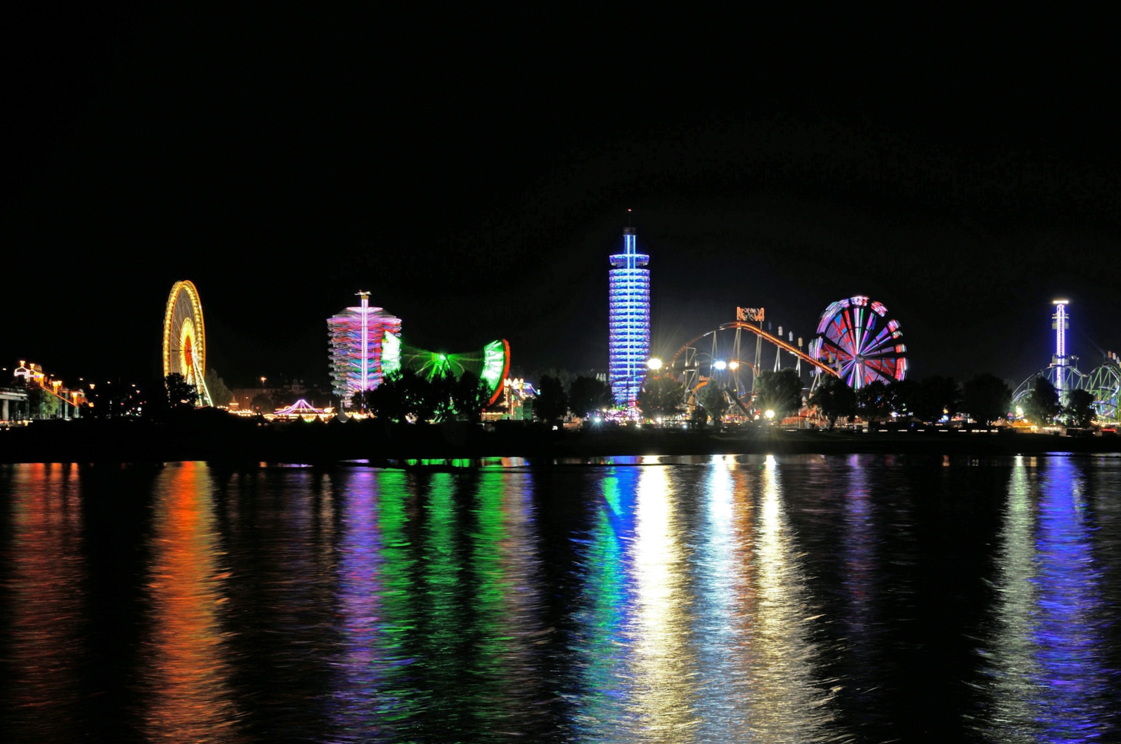 Escena nocturna de parque de diversiones con luces coloridas reflejadas en el agua