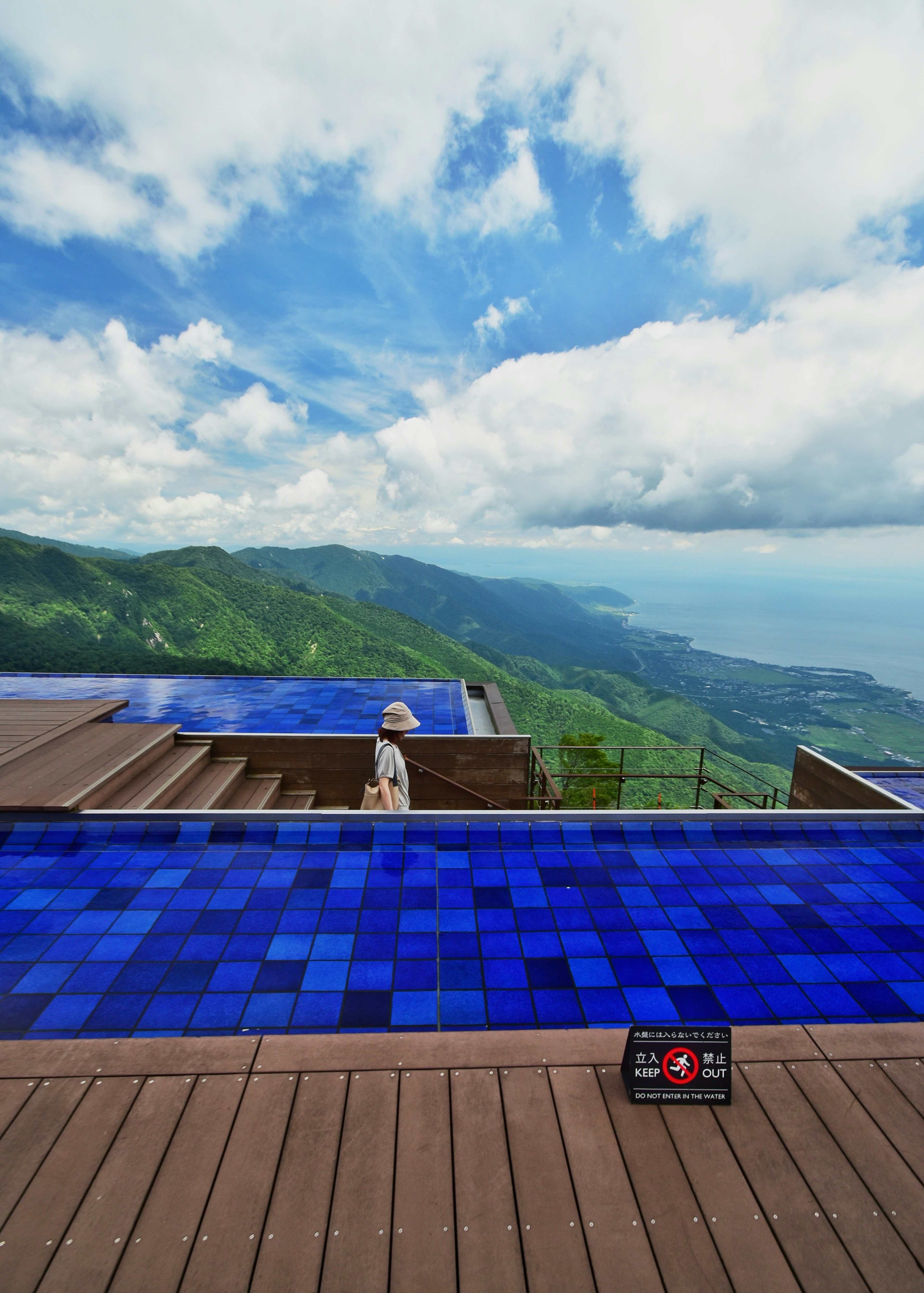 Kolam renang infinity dengan ubin biru menghadap pegunungan dan langit