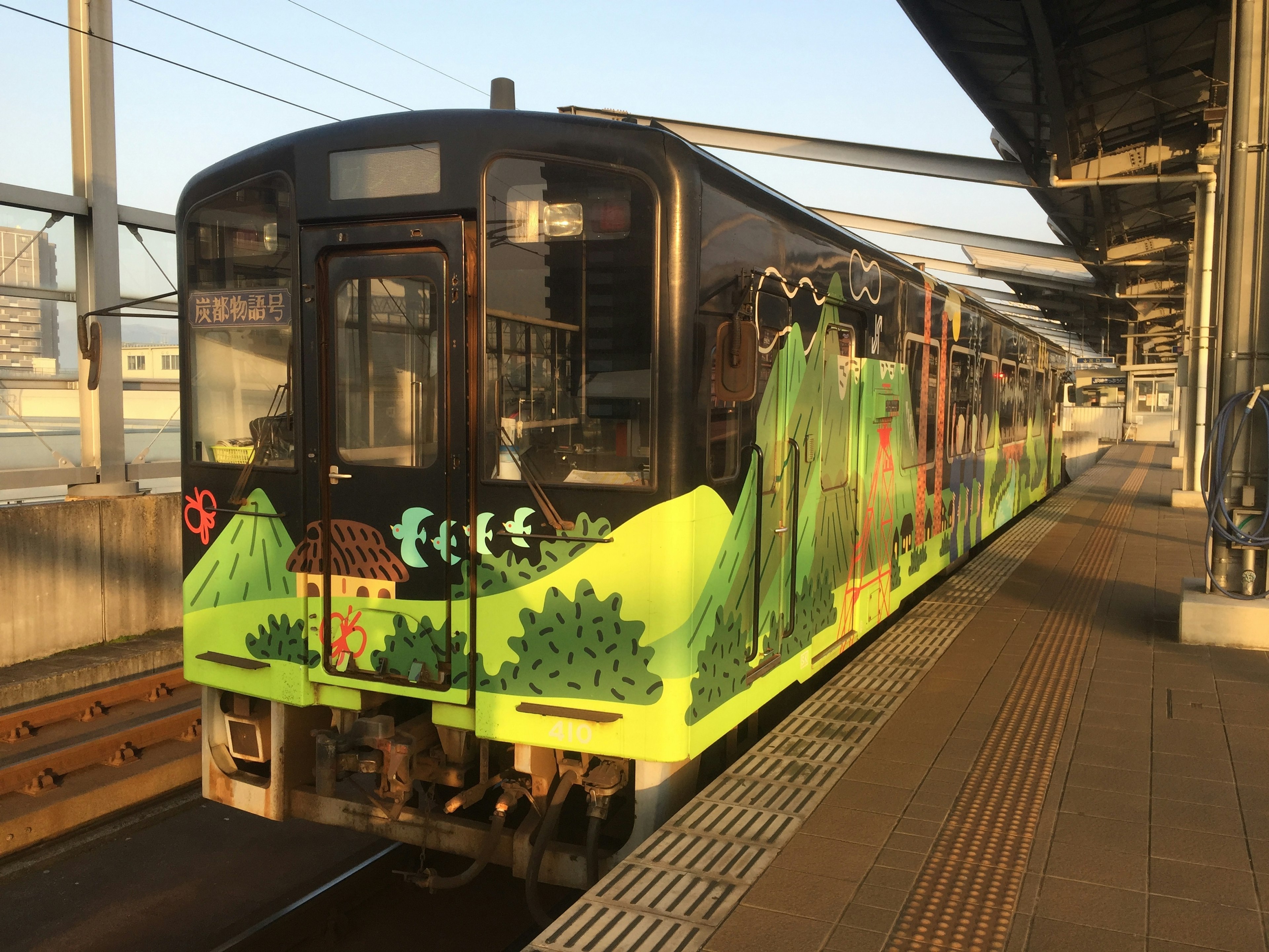 Train decorated with green landscape graphics at a station