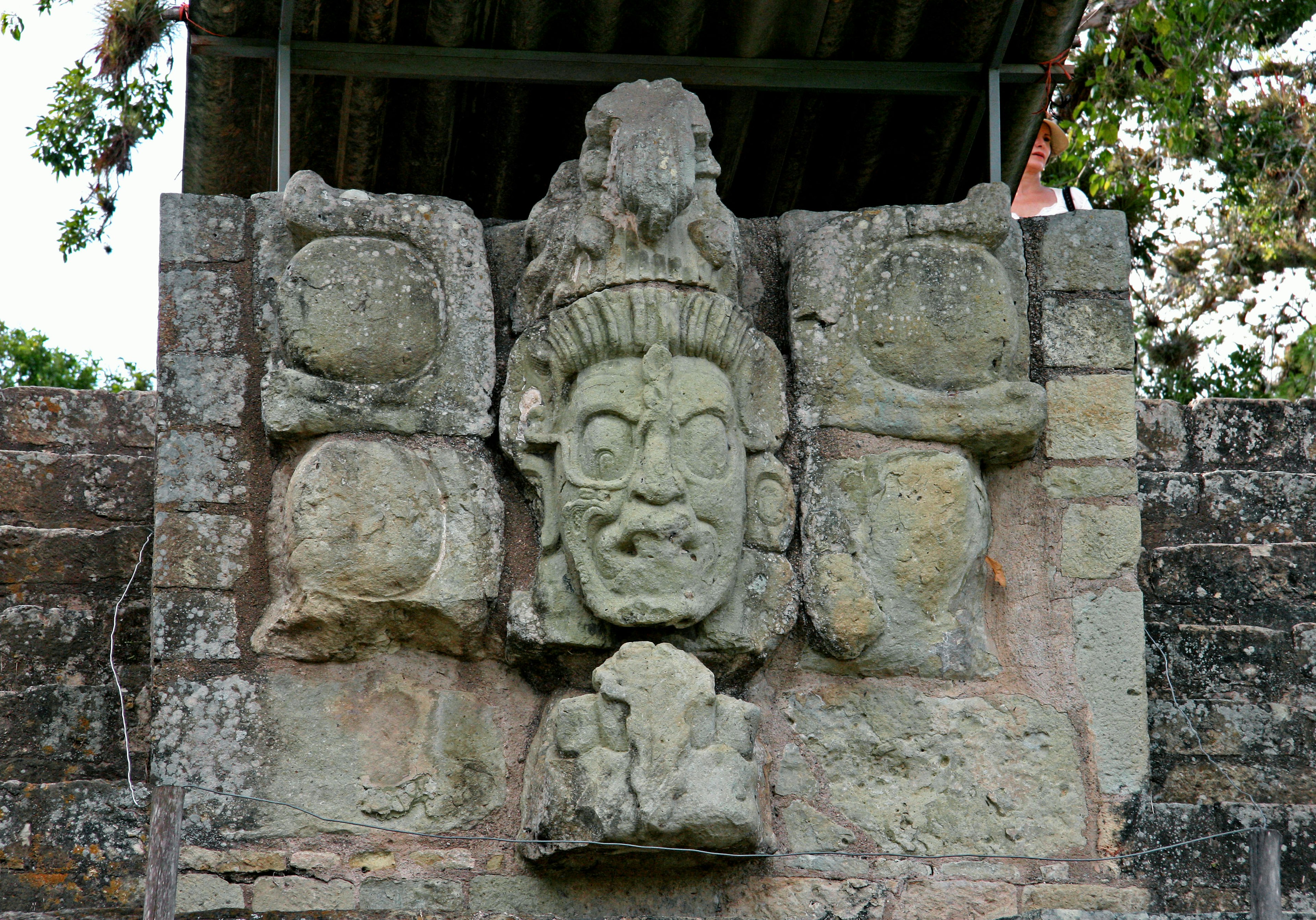 Antica parete di pietra con una prominente scultura di volto circondata da pietre decorative