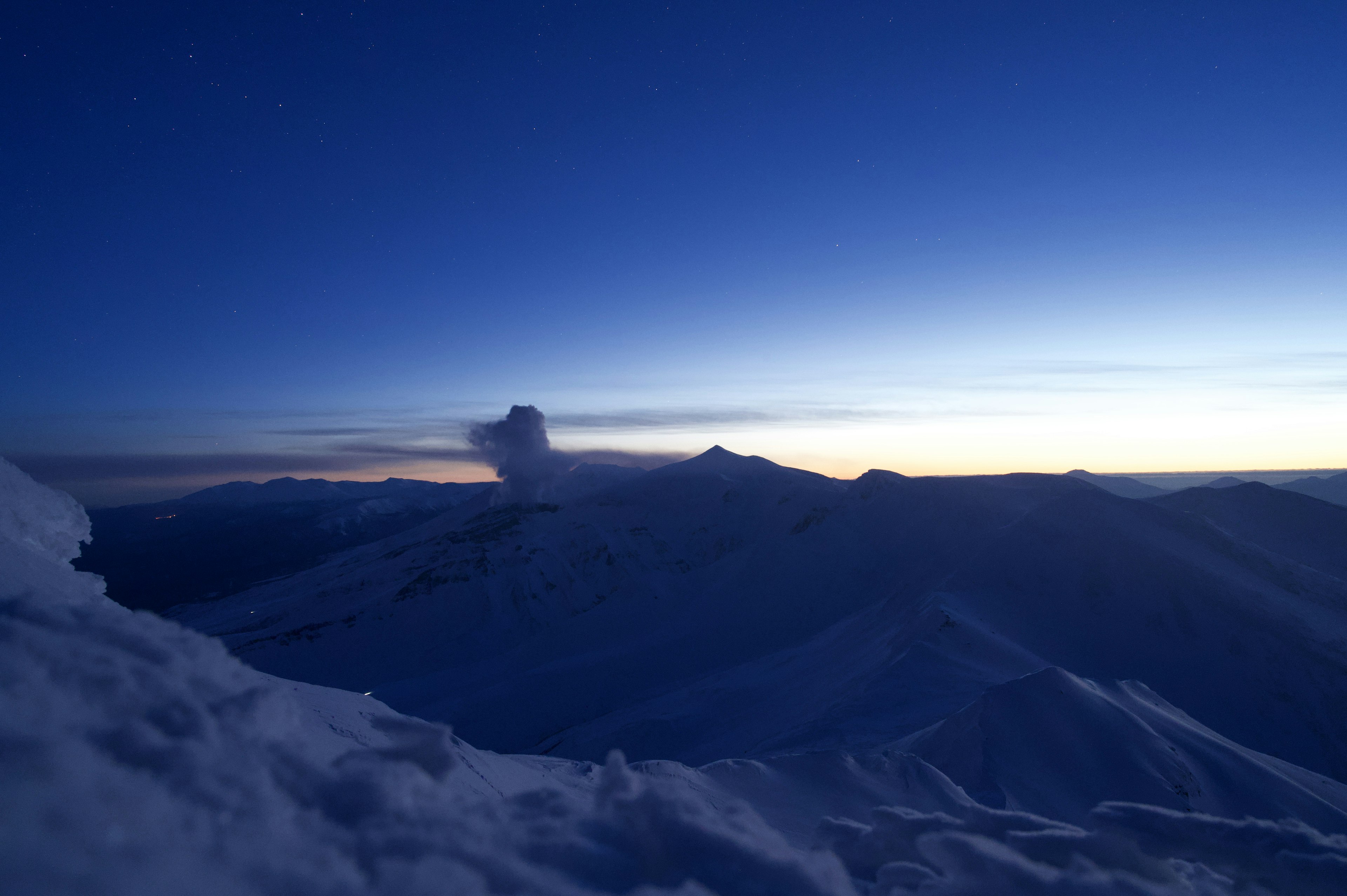 Snow-covered mountains under a deep blue sky at twilight