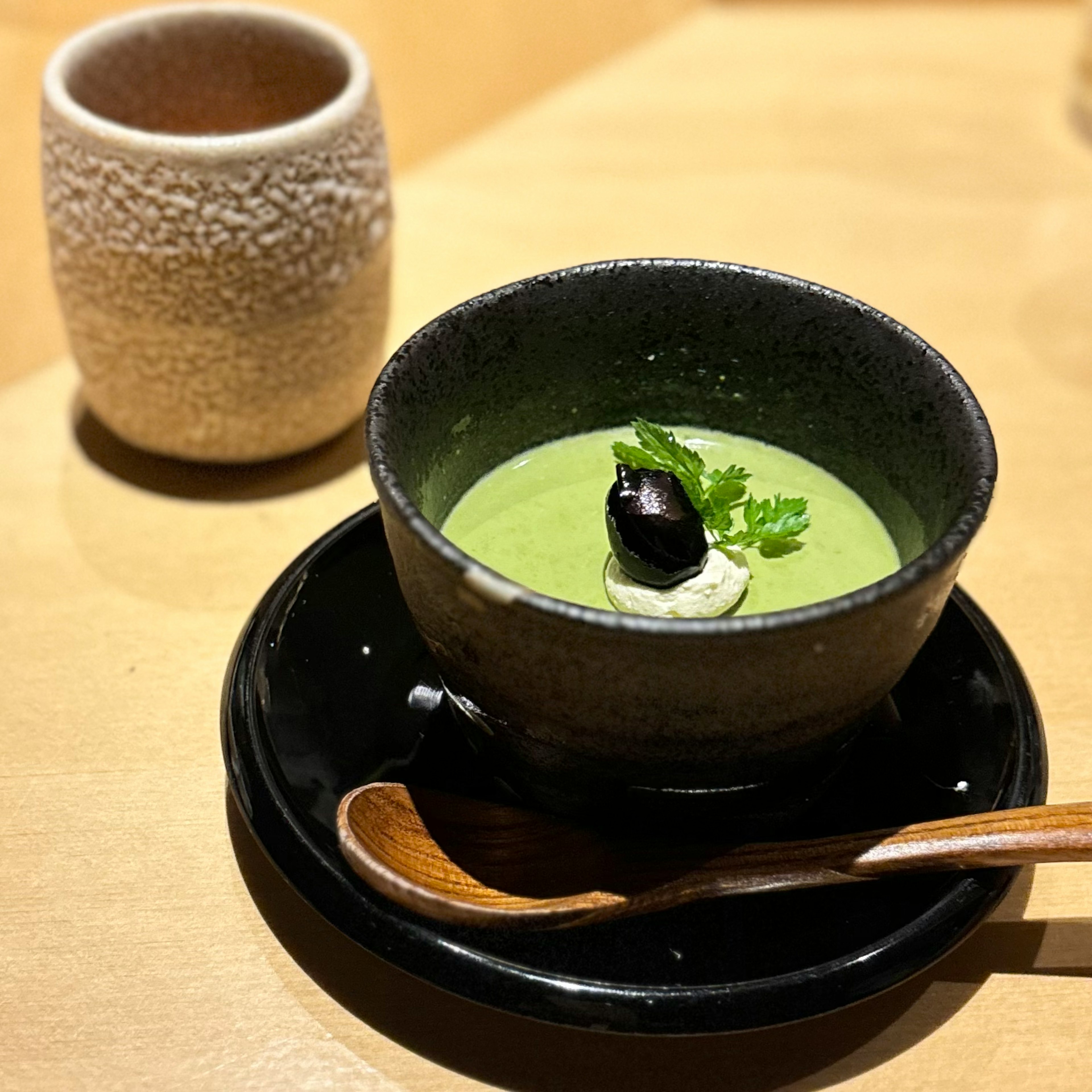 Soupe de matcha servie dans un bol noir avec une tranche de truffe noire et garnie d'herbes