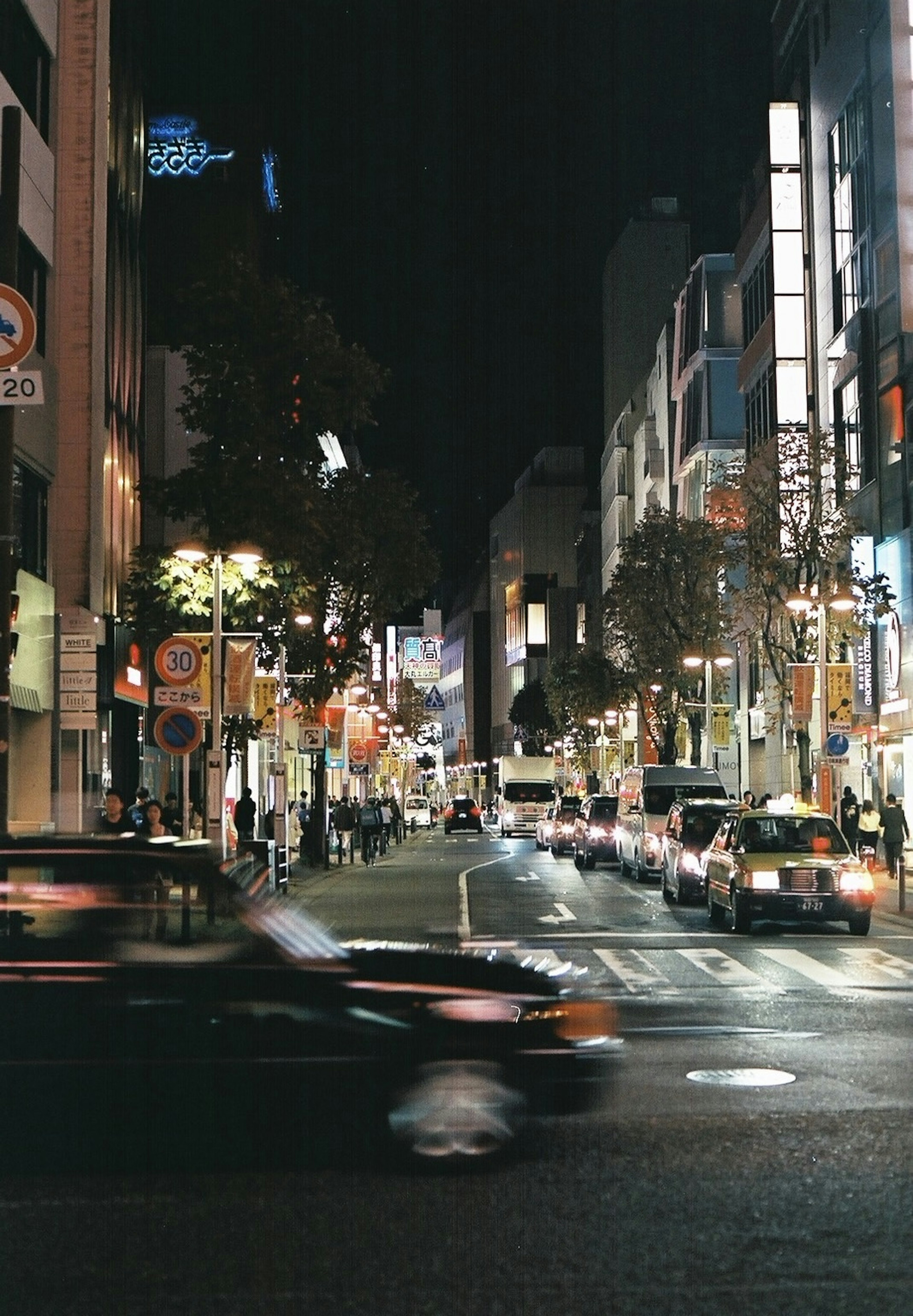 Paisaje urbano nocturno con calle concurrida y coches en movimiento