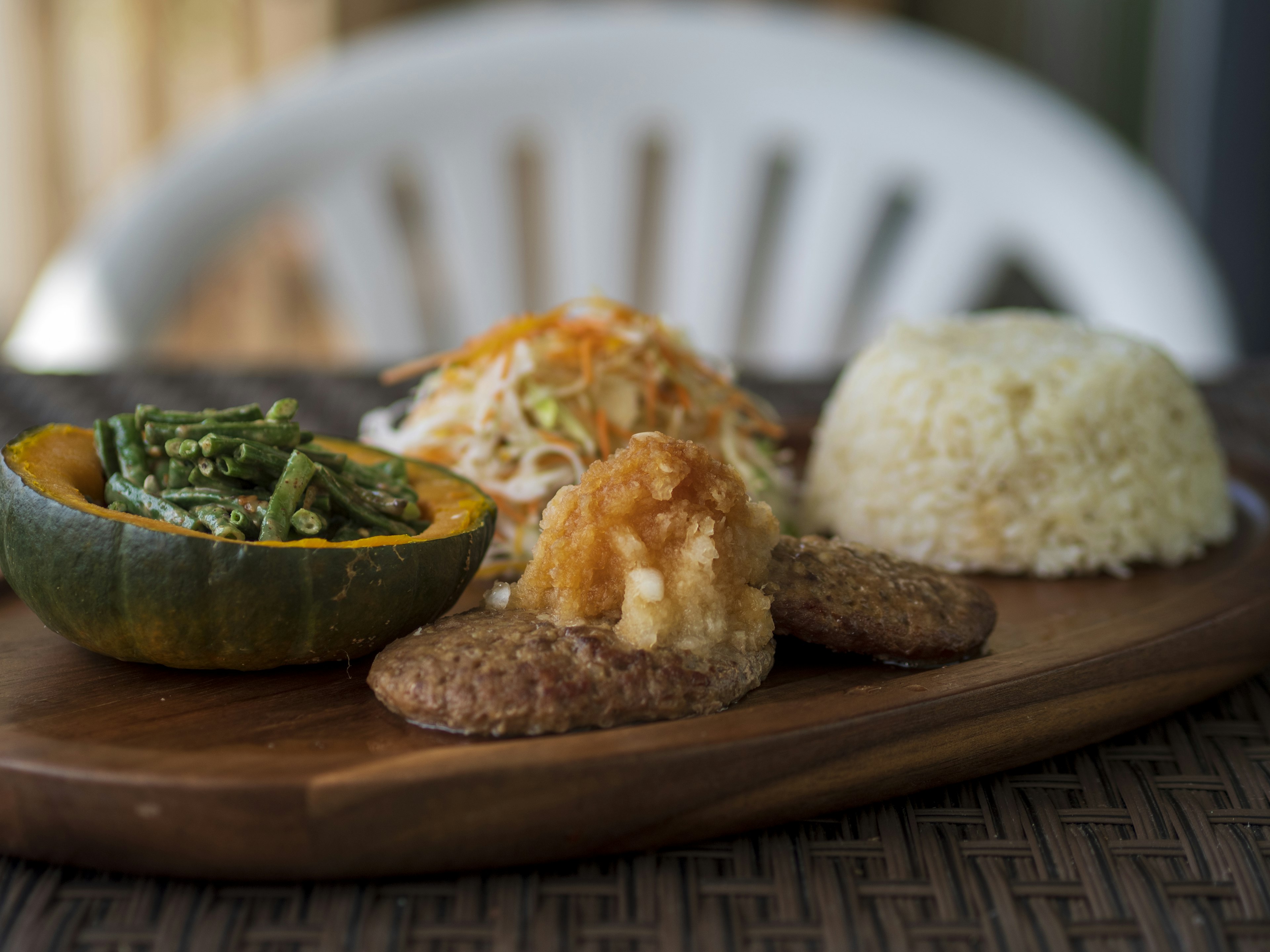 A wooden plate featuring a variety of dishes including green vegetables pumpkin fried chicken and rice