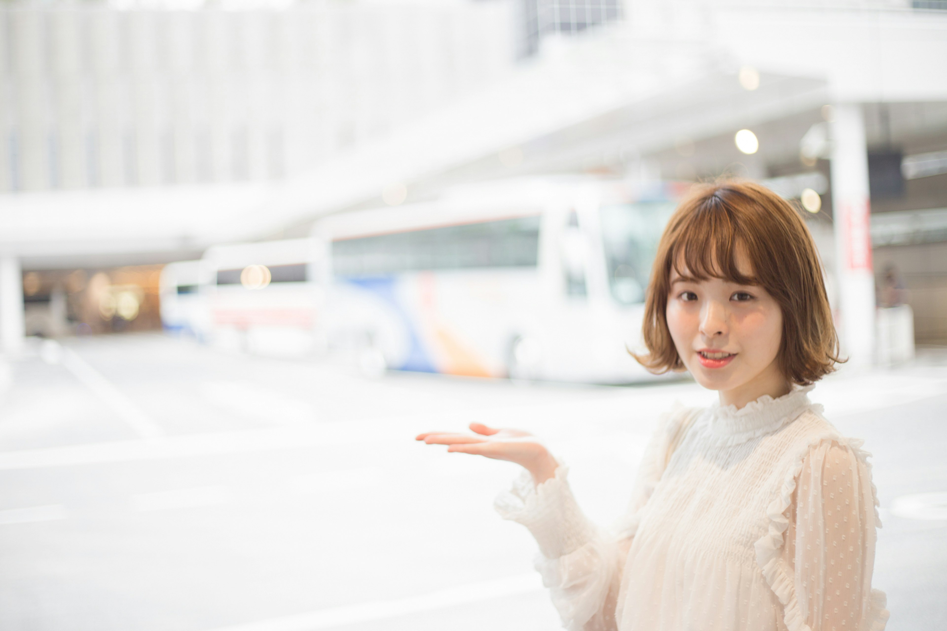 A woman gesturing with her hand in a bright setting with a bus in the background