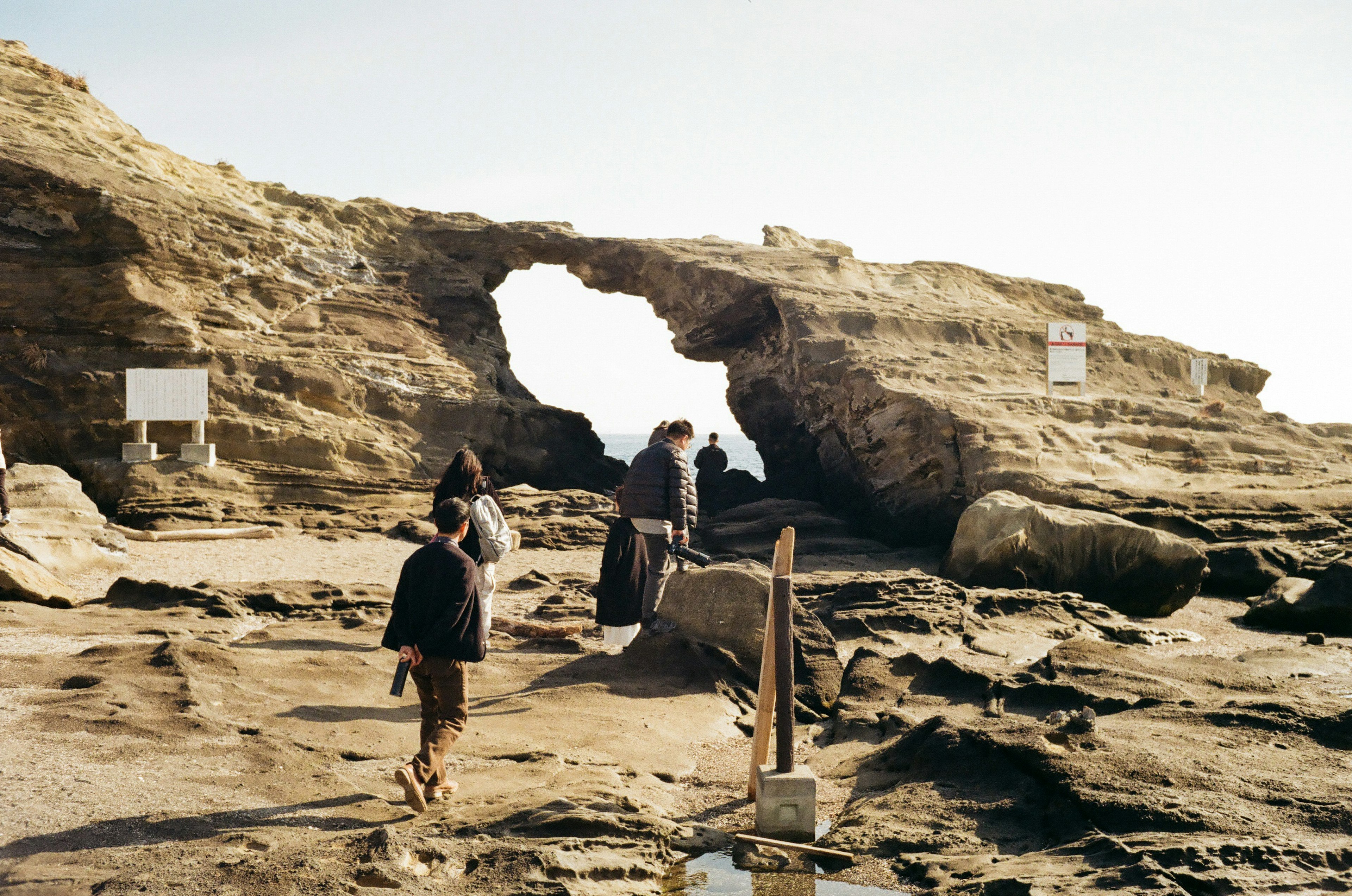 Persone che camminano vicino a un arco di roccia naturale su una costa rocciosa