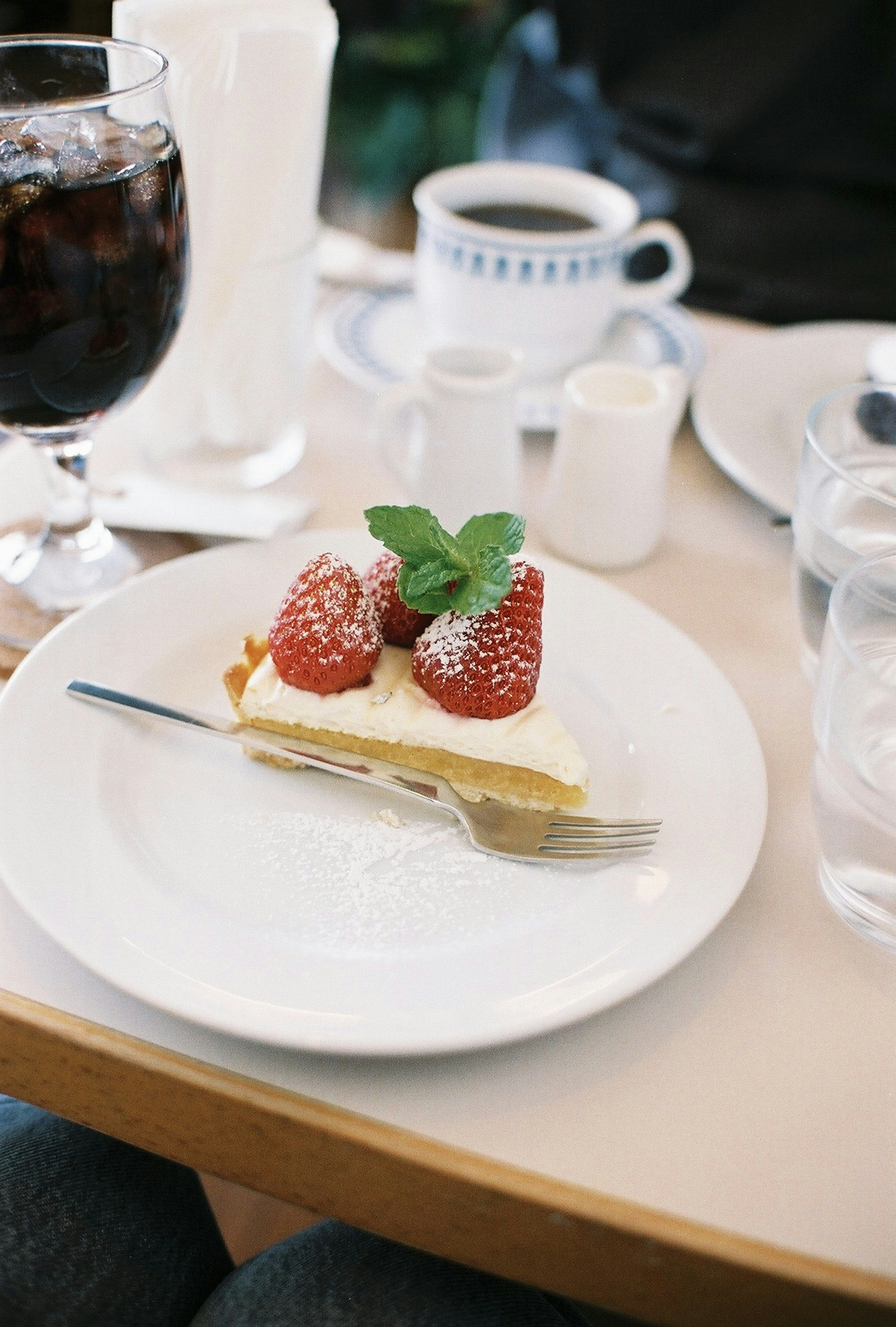 Teller mit Dessert, garni mit Erdbeeren und Minze, mit einer Gabel daneben