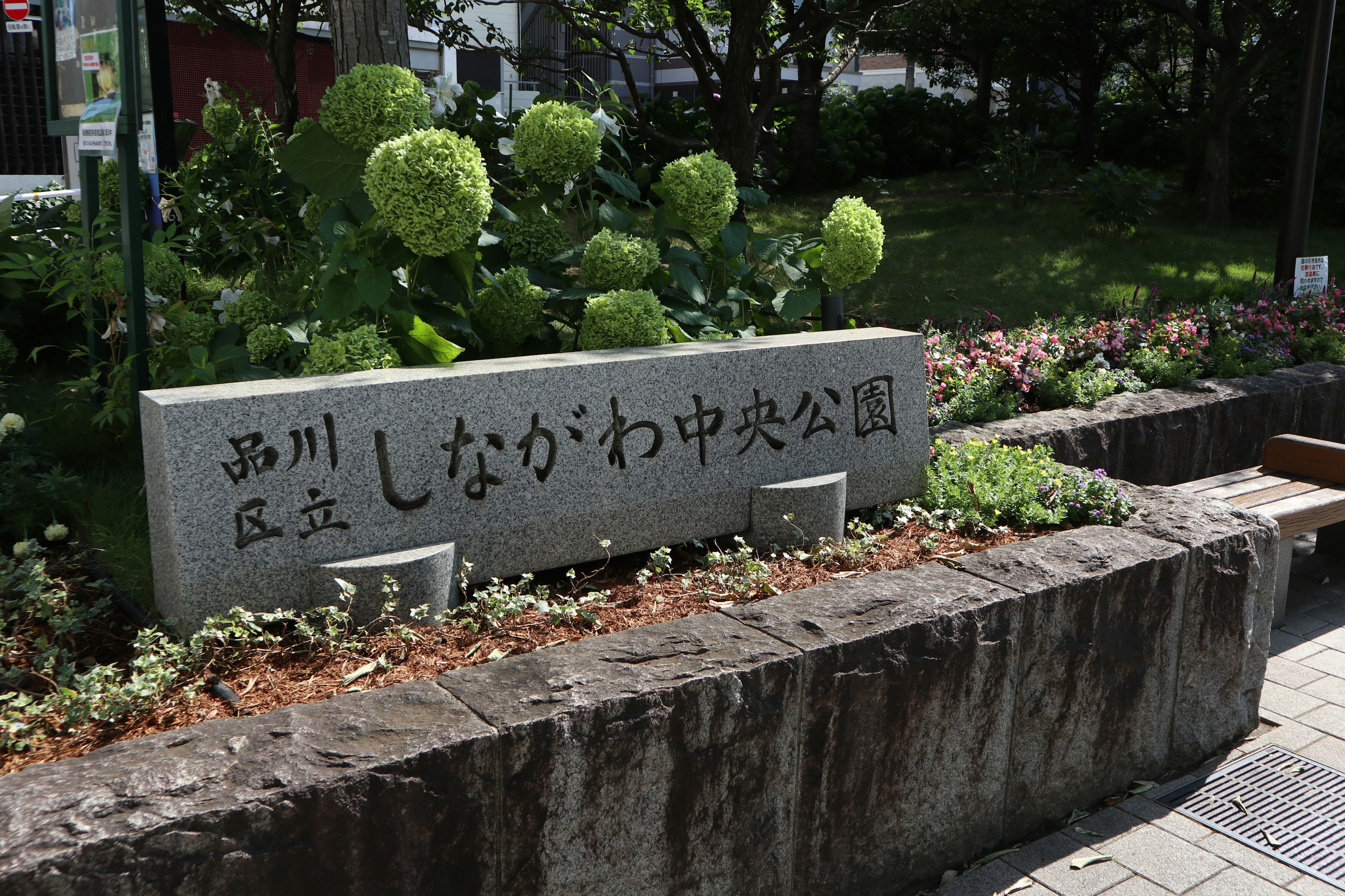 新川中央公園の石の看板が緑の植物の前に立っている