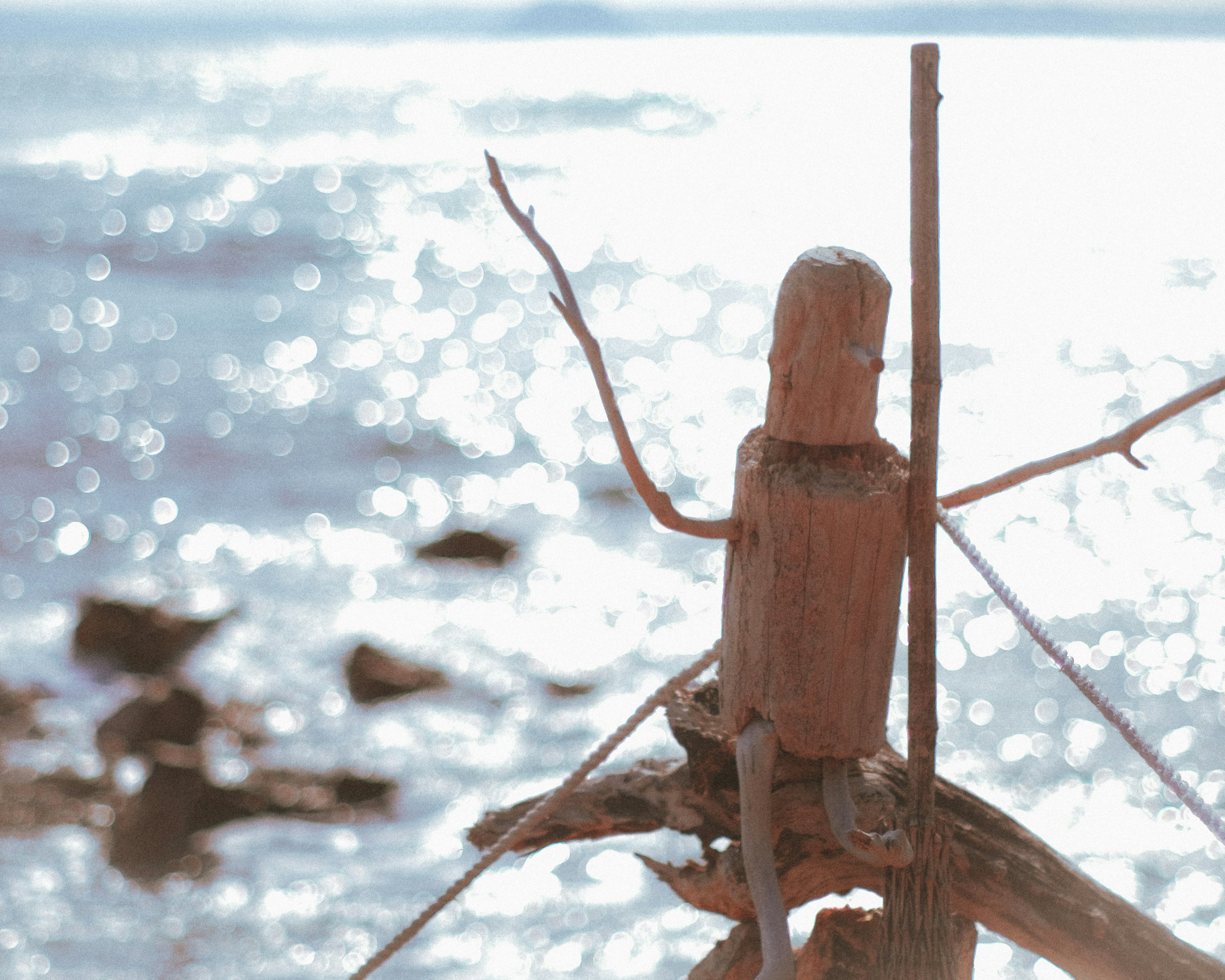 A wooden sculpture figure stands by the sea with sparkling water in the background